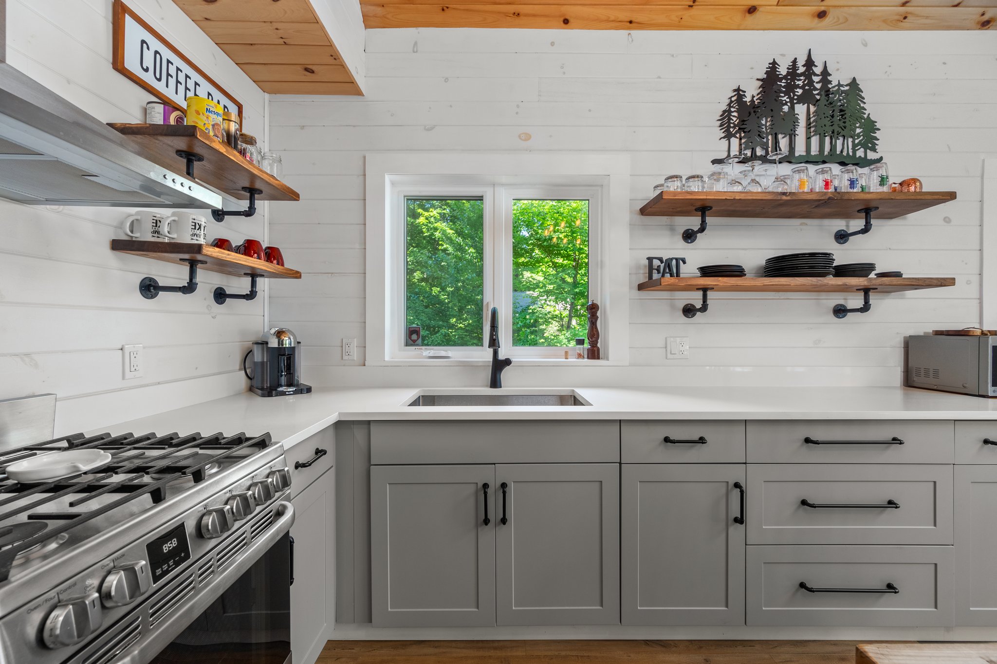 To the left, a stove. Perpendicular, lower grey cabinets and a kitchen sink with a window above