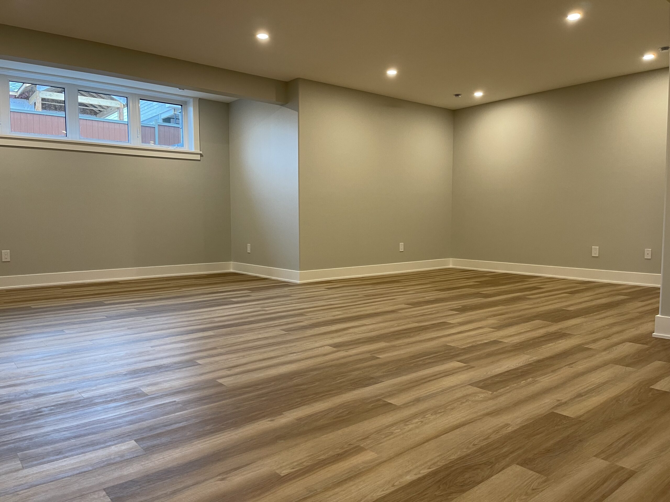 A large empty room with wood floors and pot lights