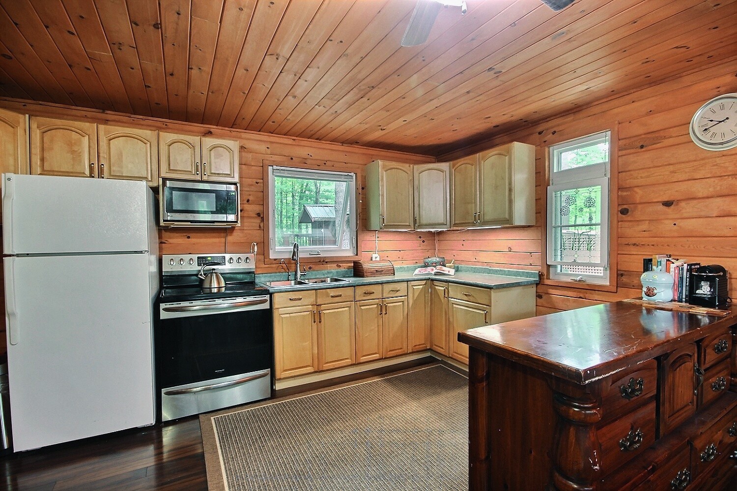 A fridge, stove, and wood cabinets along a wood panelled wall