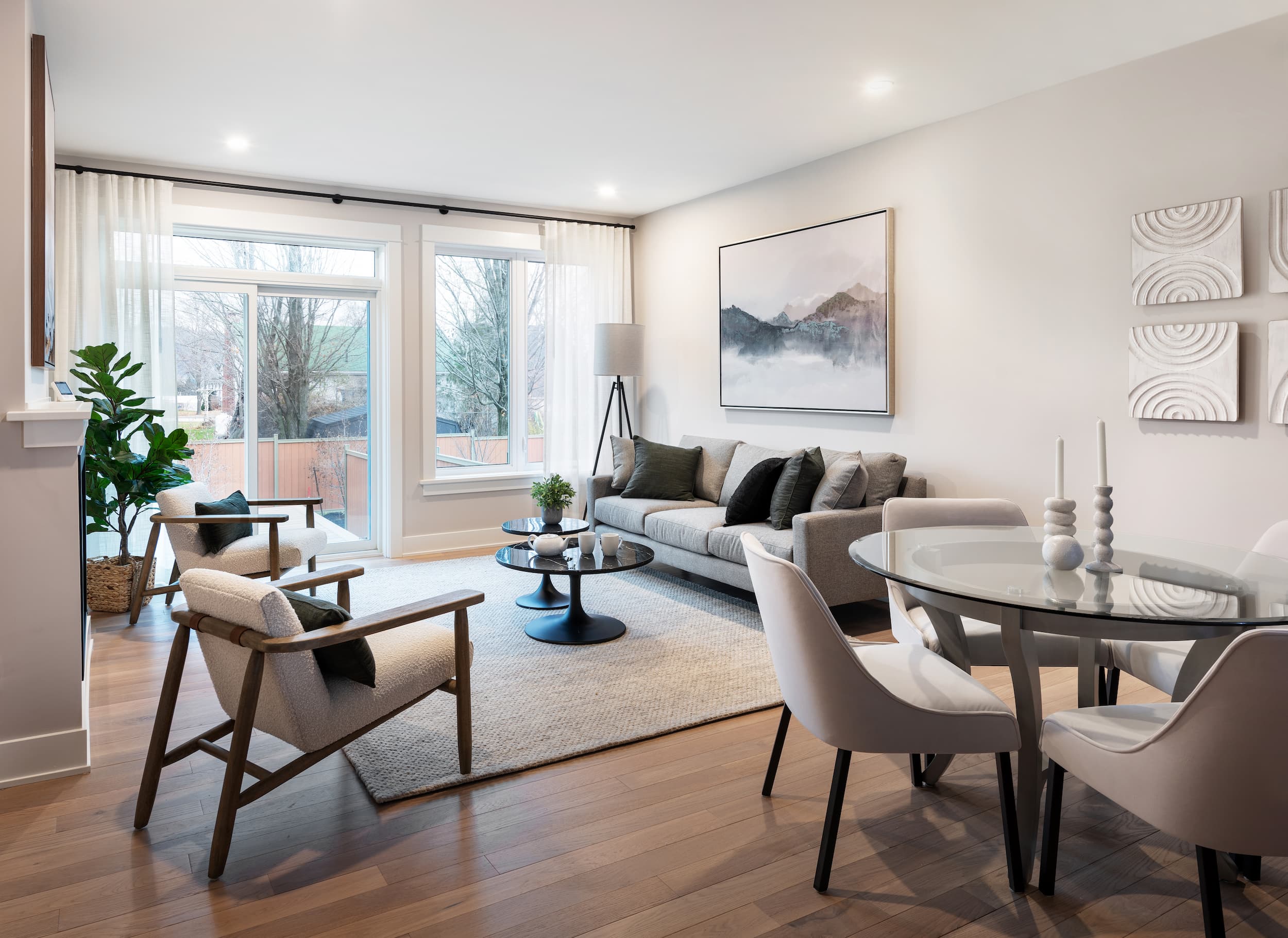 An open concept living space with a white couch facing two white chairs on a cream coloured rug