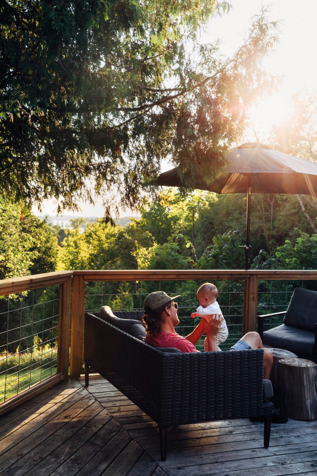 a man in a hat holds a young baby on a cottage deck