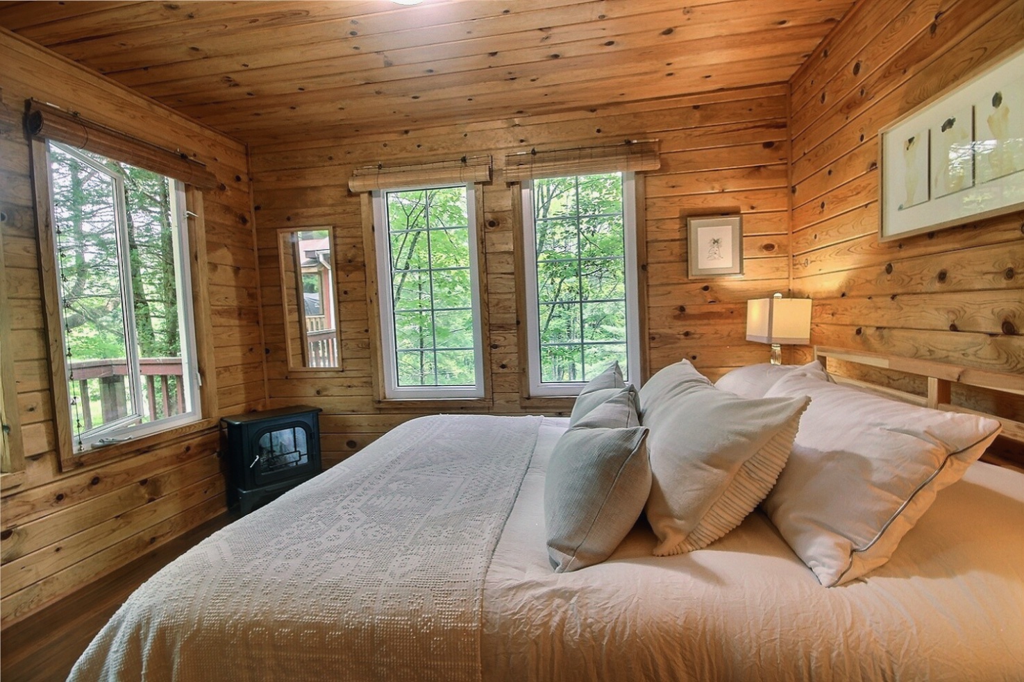 The side of a large white bed with three pillows in a wood panelled room with windows on two sides