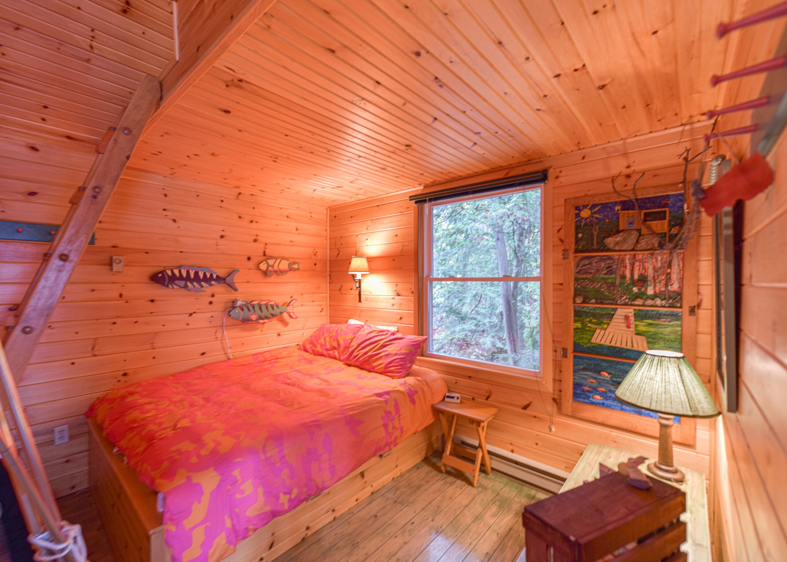 A pink bed in a wood panelled room beside a large window