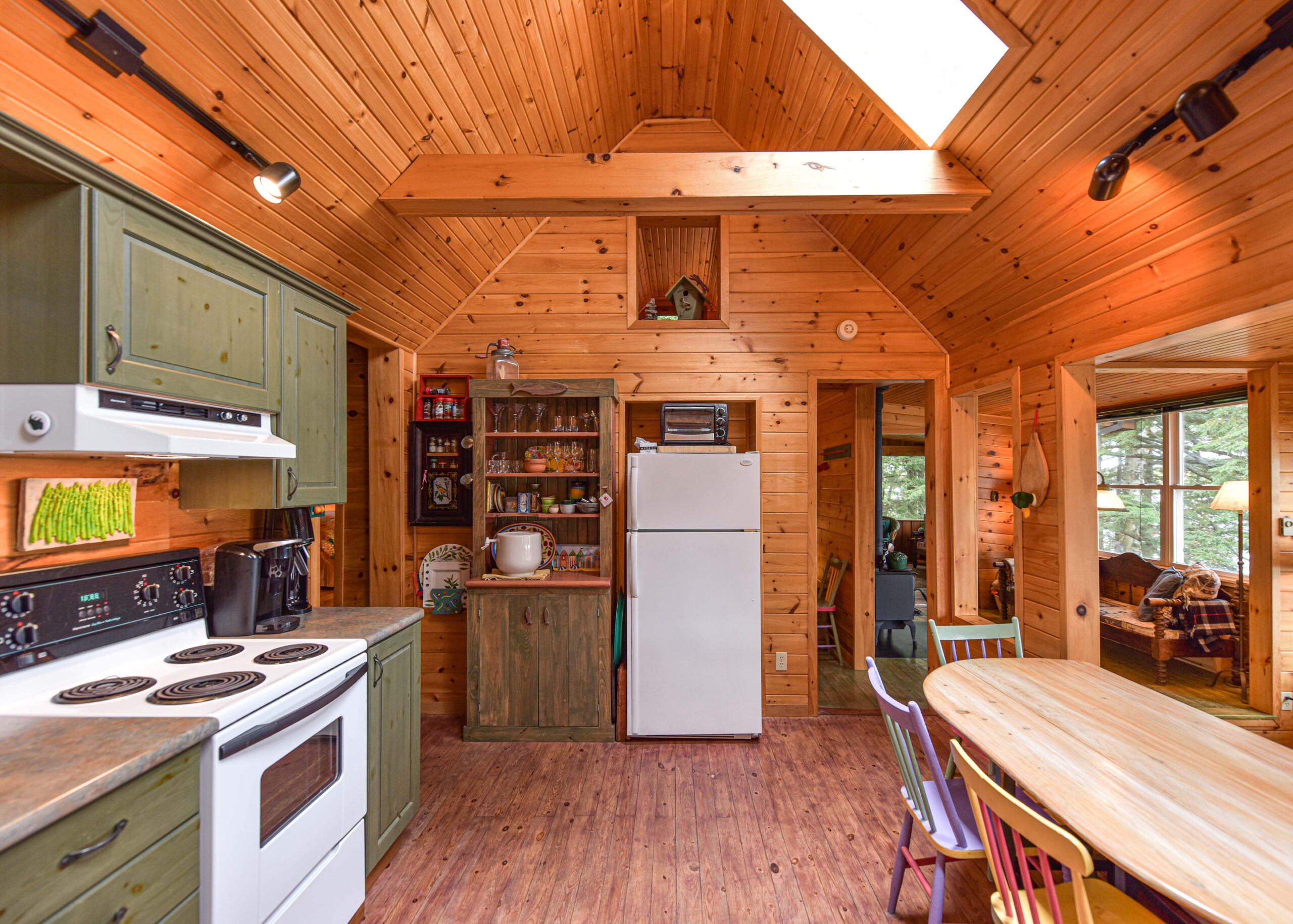 Green kitchen cabinets face a round wood table. In the middle, a white fridge