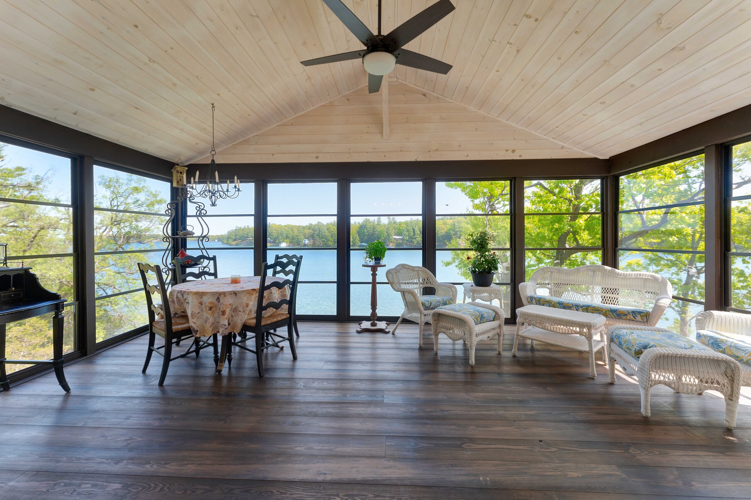 A spacious room with dark wood floors, panoramic views of the water, and a high white ceilings