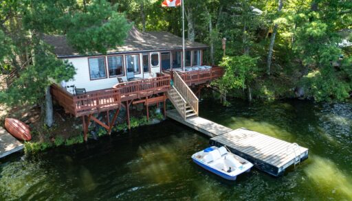 A white cottage with a red deck and a dock on the lake