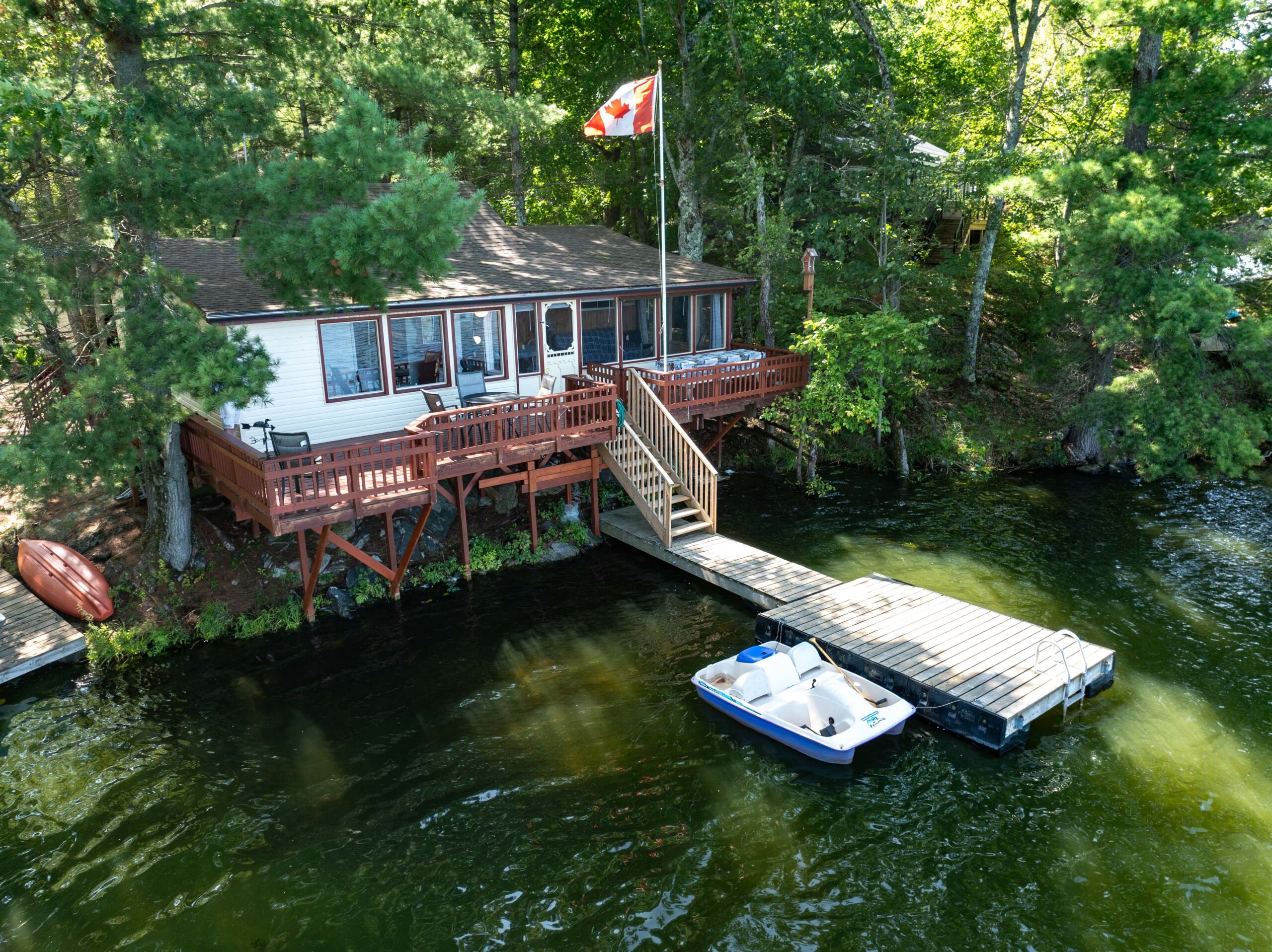 A white cottage with a red deck and a dock on the lake