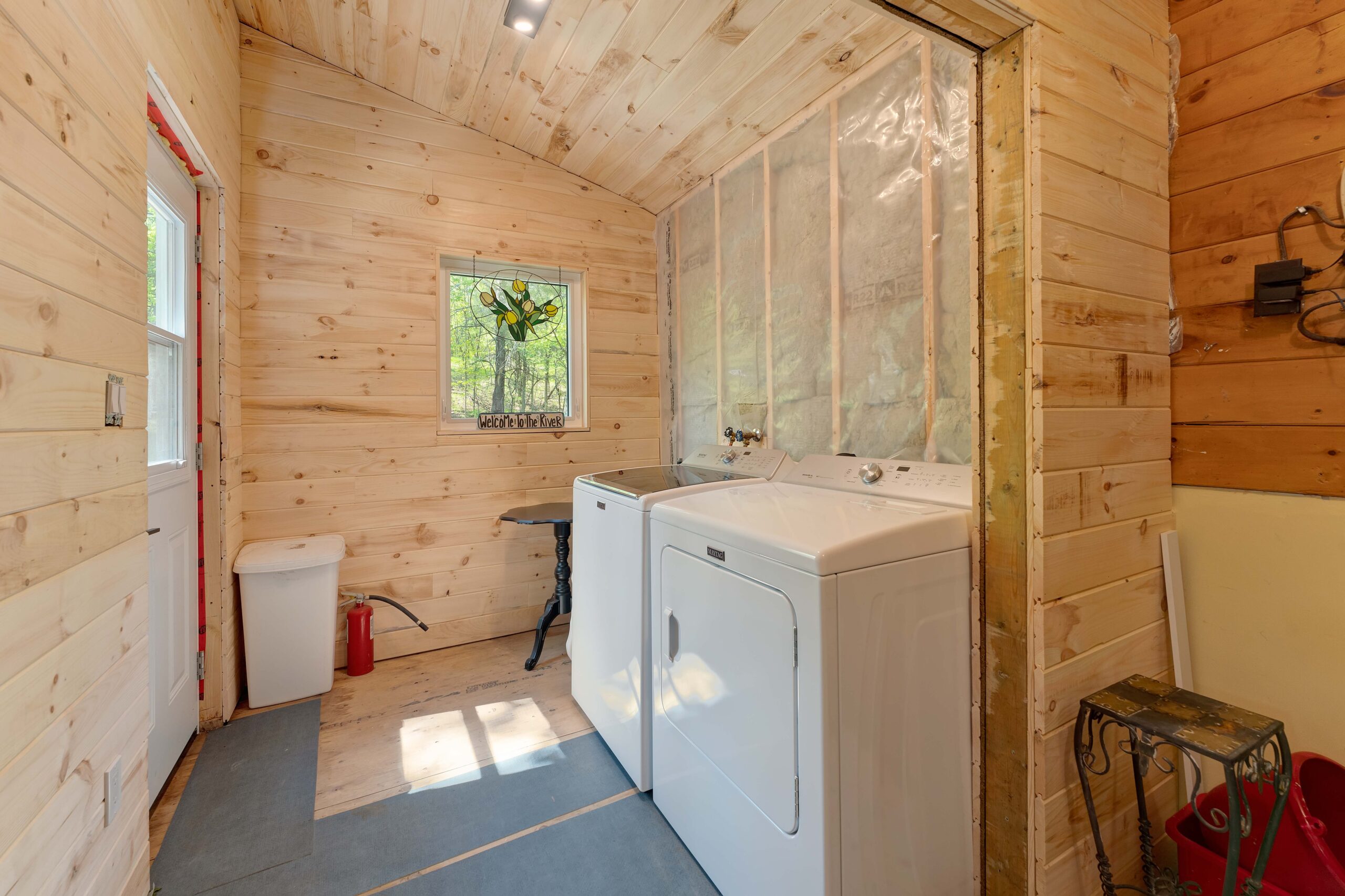 In an unfinished wood room, laundry machines sit on the floor beside each other