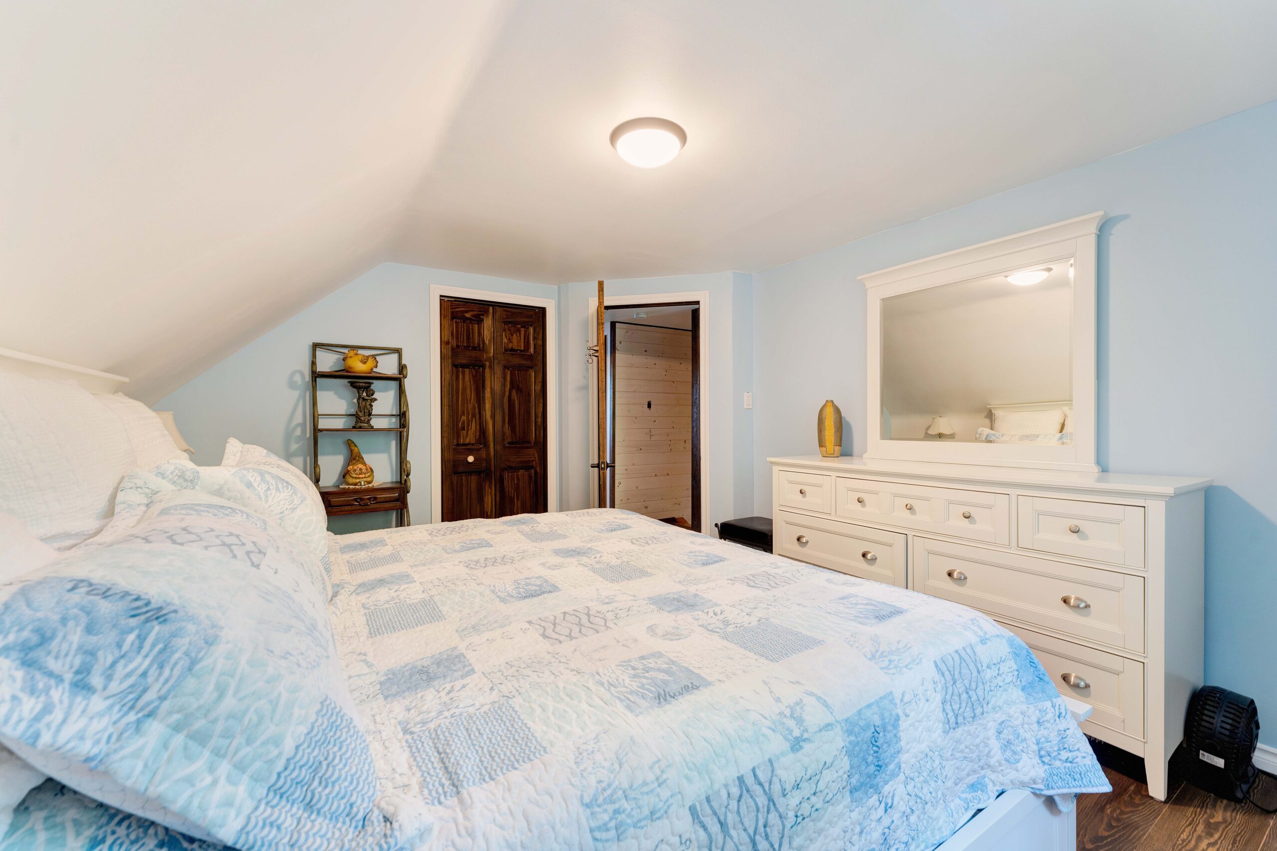A large white and blue bed in a white bedroom. faces a white dresser