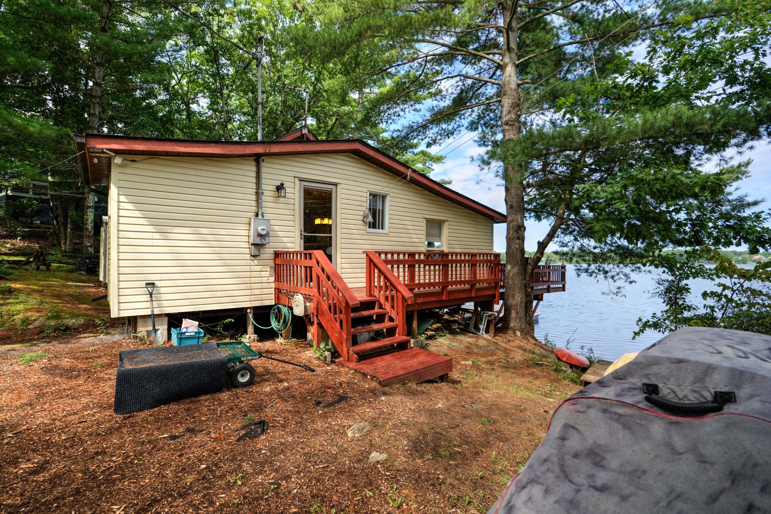 A beige paneled cottage with a red deck beside a lake