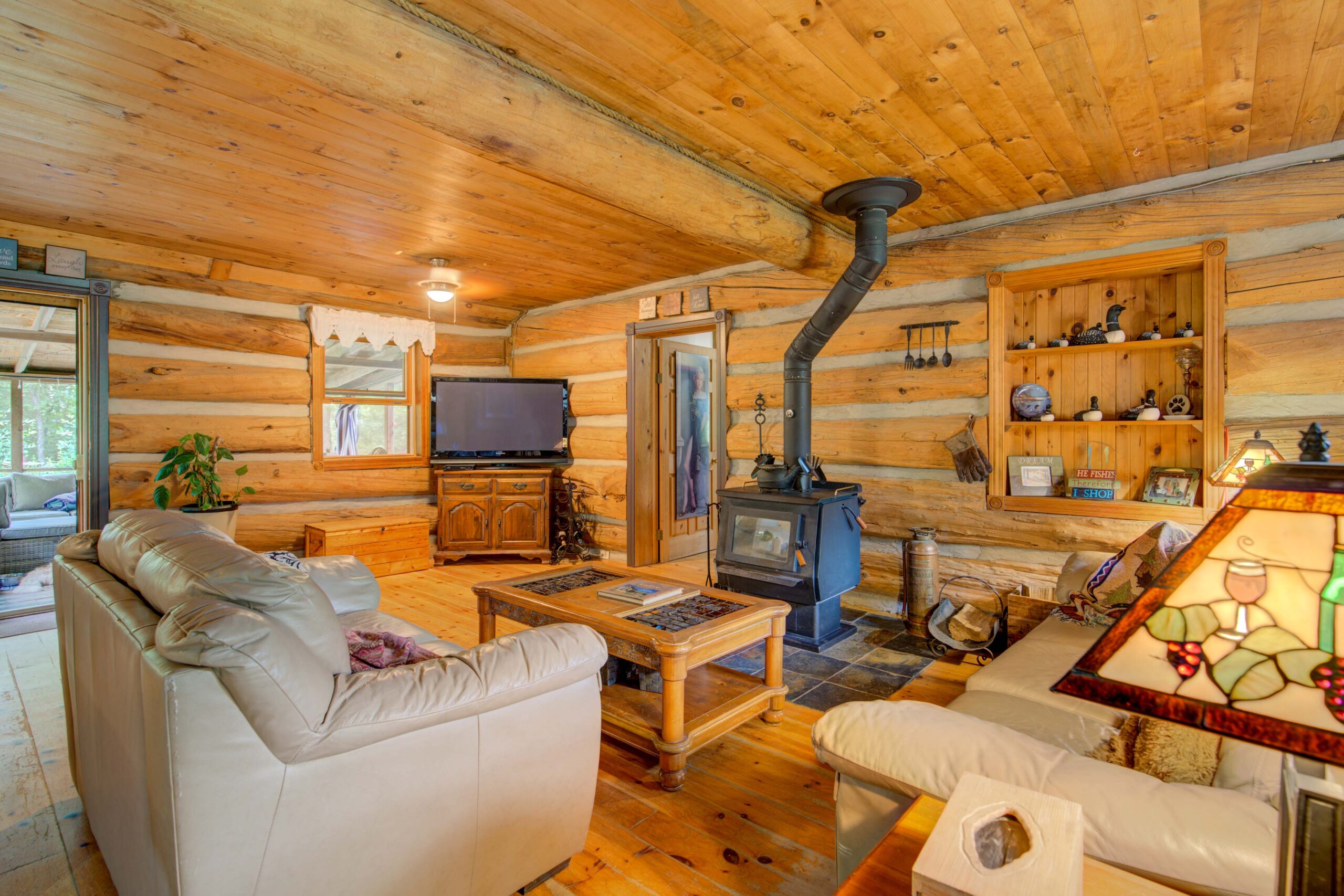 A beige couch faces a wood coffee table and a wood stove in a wood-paneled room