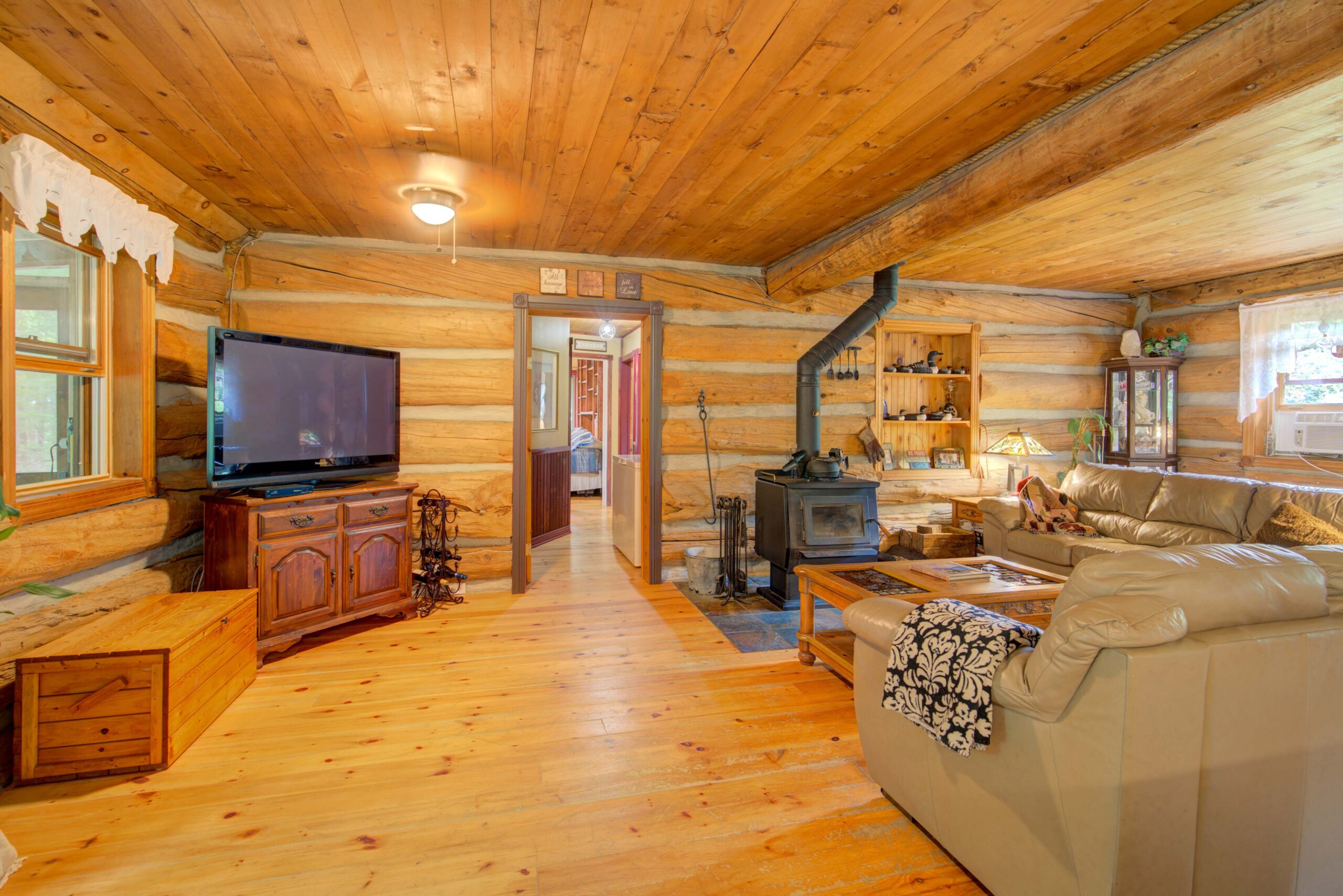 A beige couch faces a wood coffee table and a wood stove in a wood-paneled room