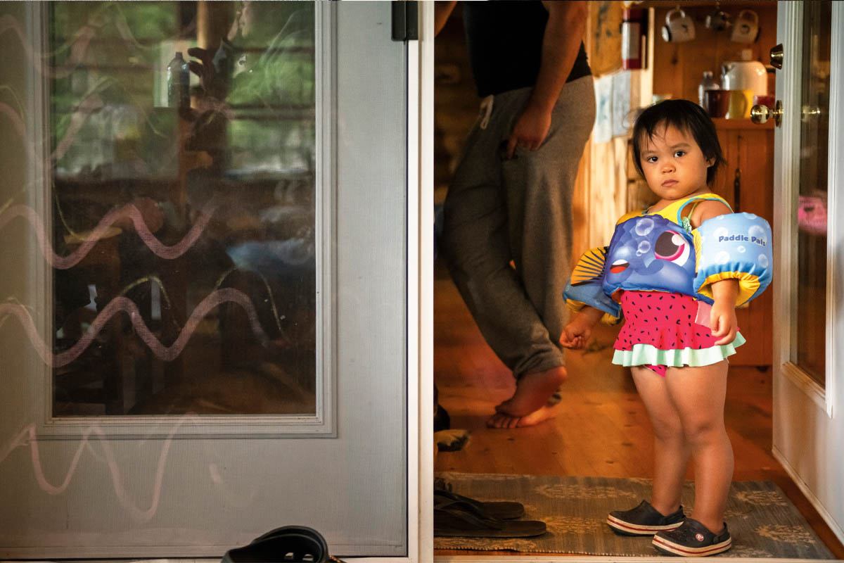 A young child stands in the door in a bathing suit and floaties