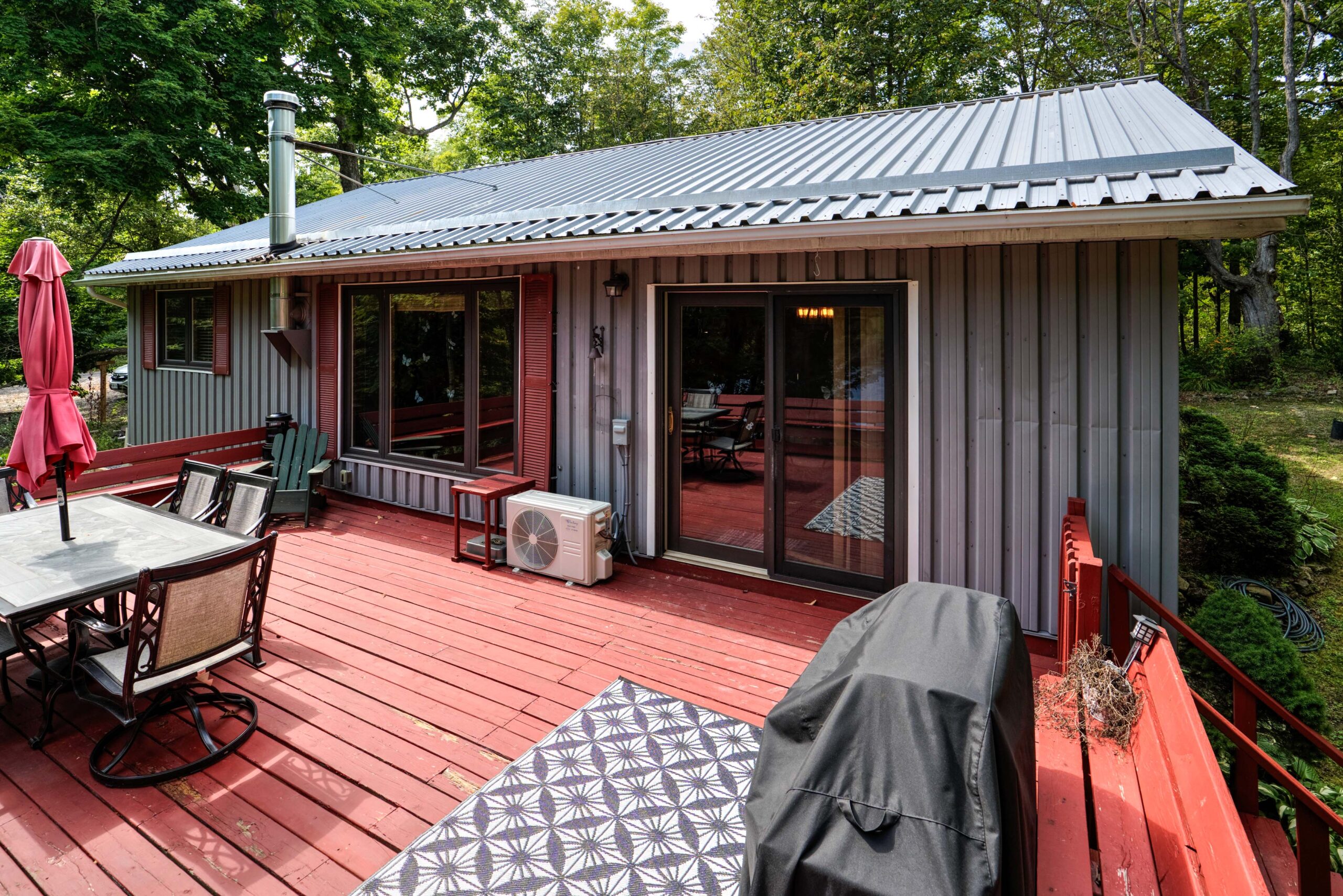 A red deck with a BBQ and patio furniture attached to a grey cottage