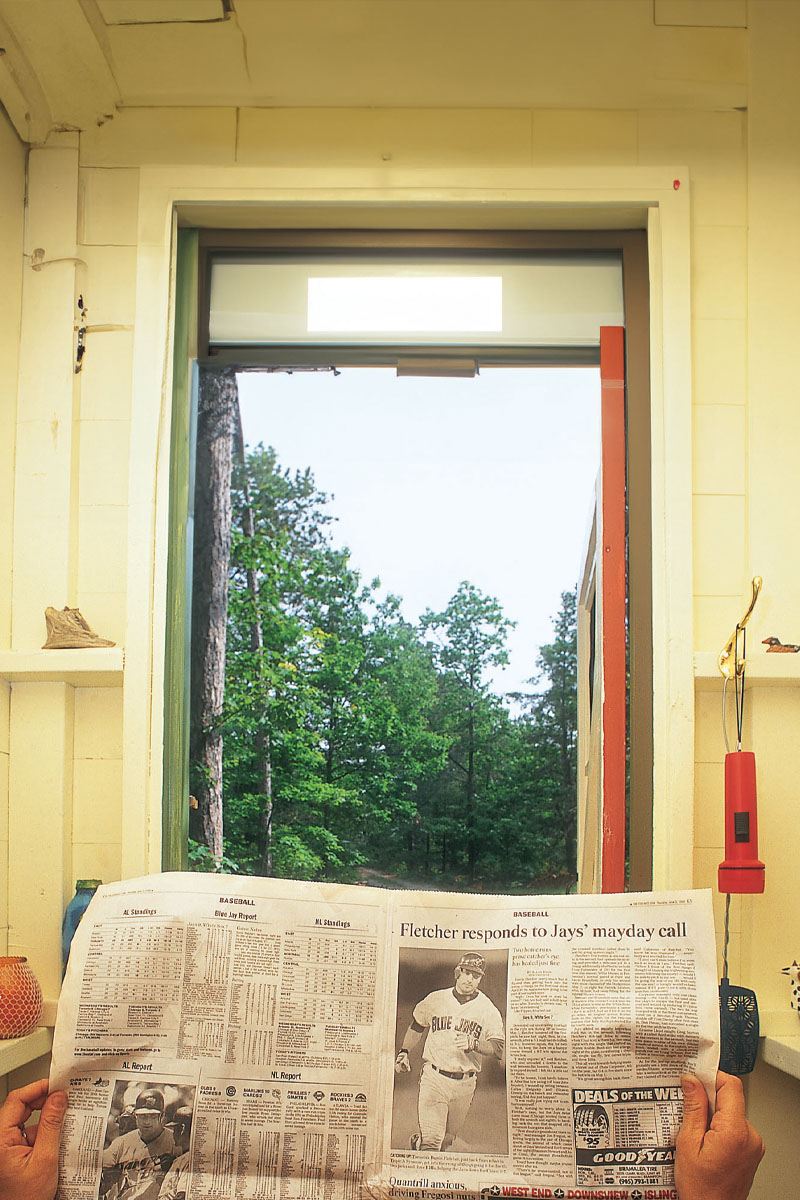 Looking outside from inside an outhouse while a man holds up a newspaper