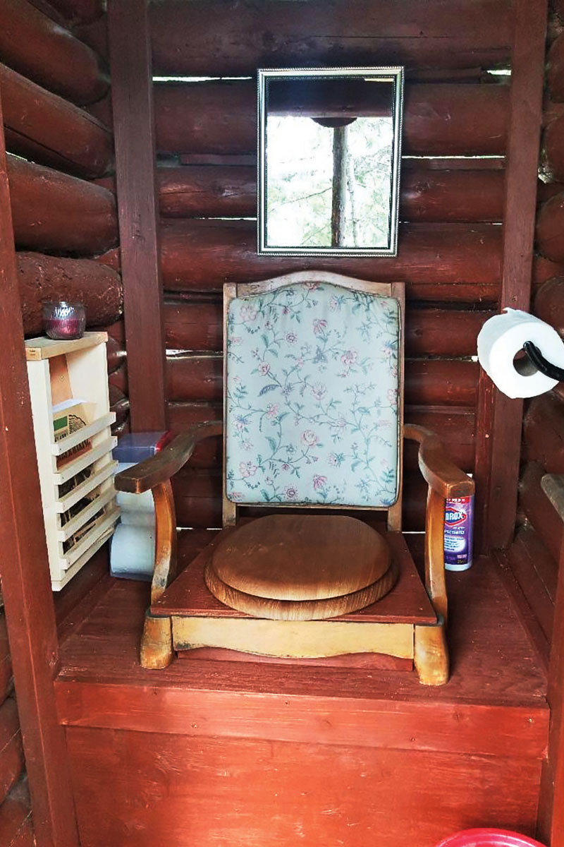 The interior of an outhouse with an old chair fashioned into a throne for the seat