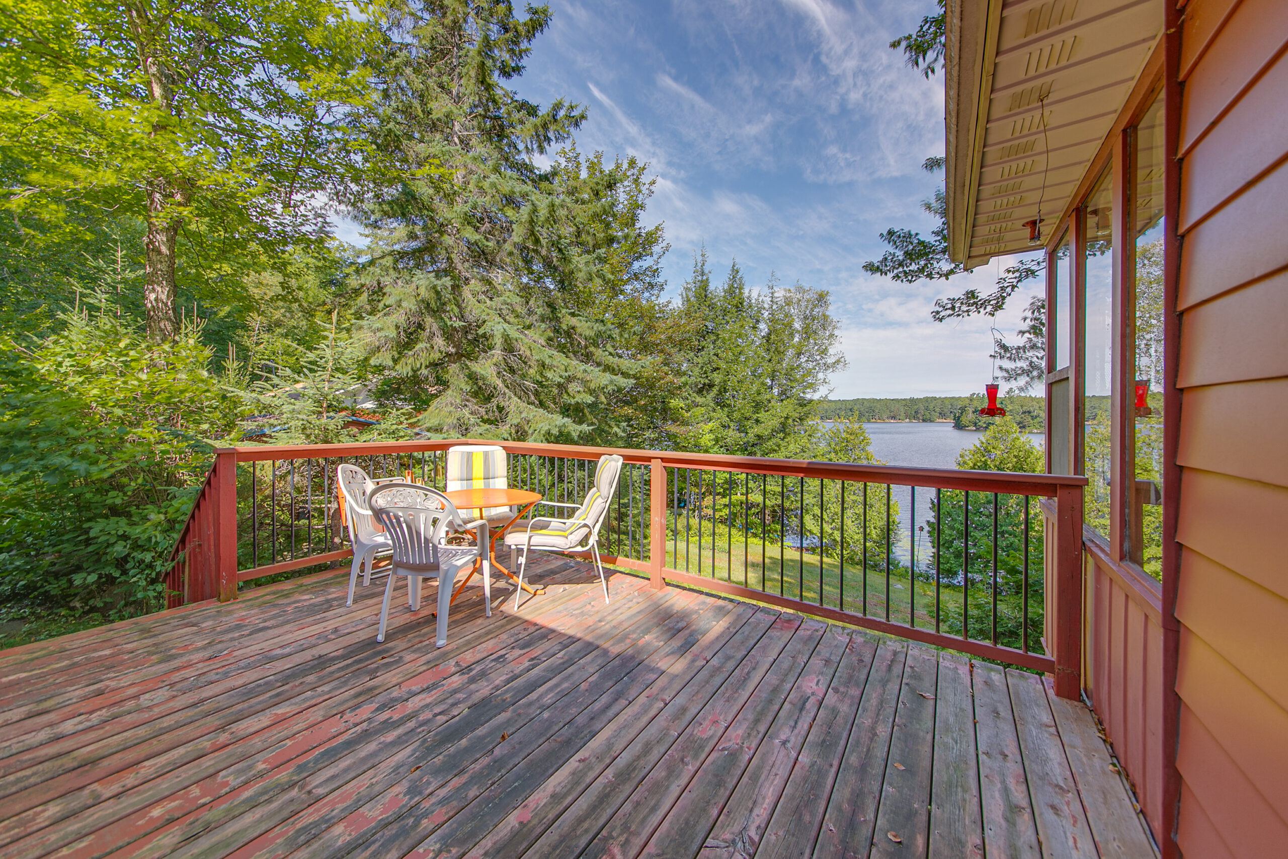 A brown and red deck with a small dining area faces the lake