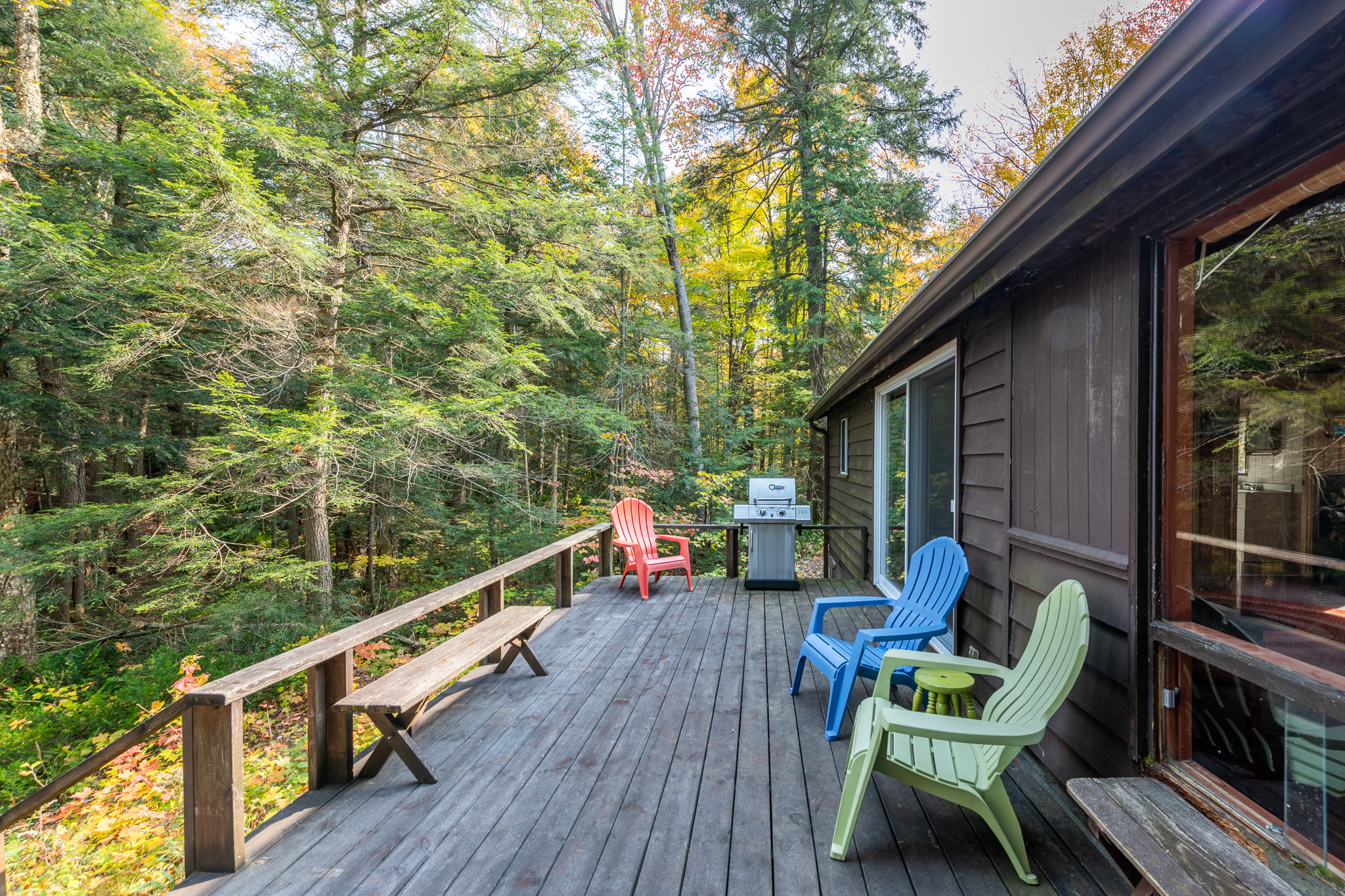 A brown-grey deck with colourful Muskoka chairs