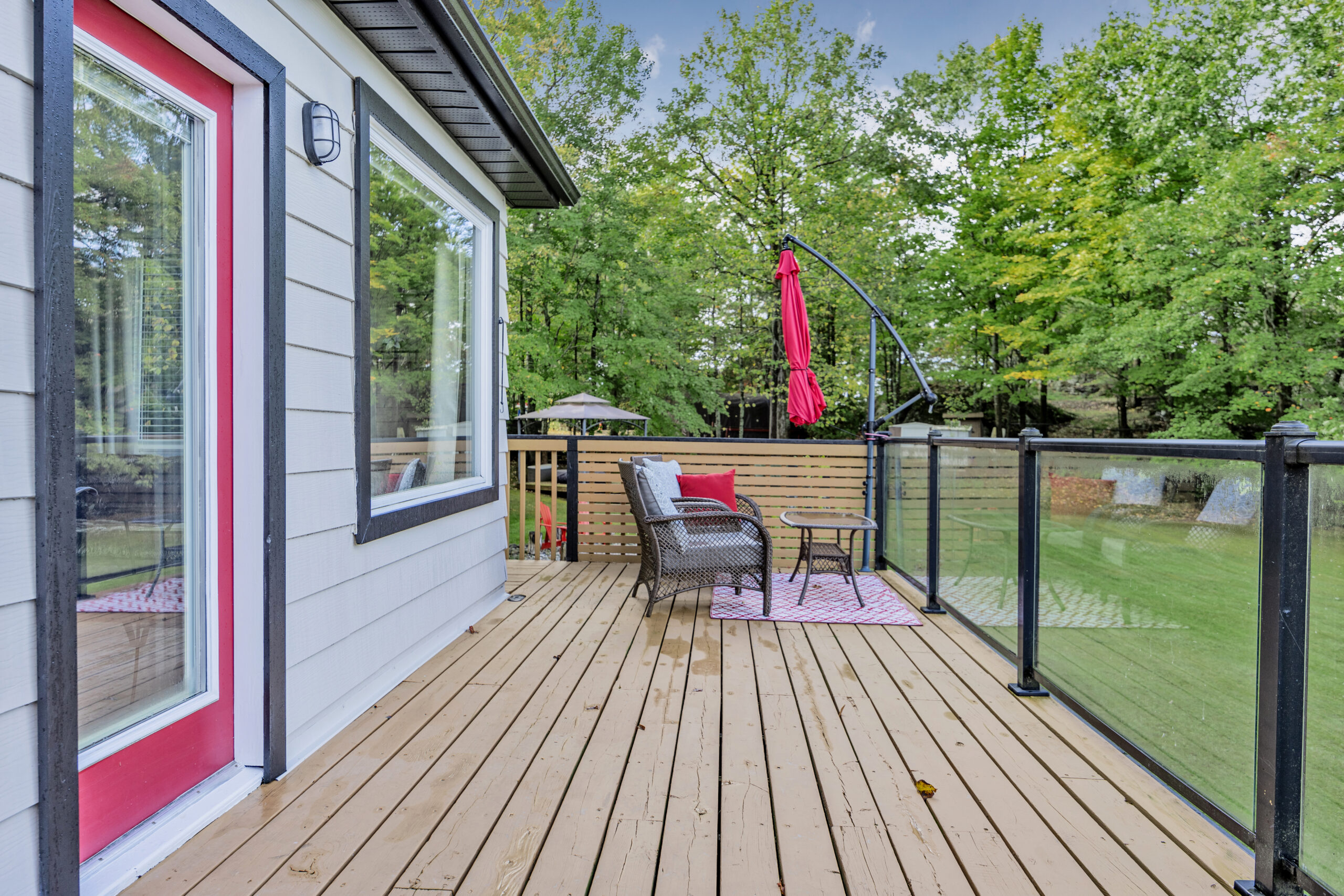 A small white cottage with a brown deck and a red door