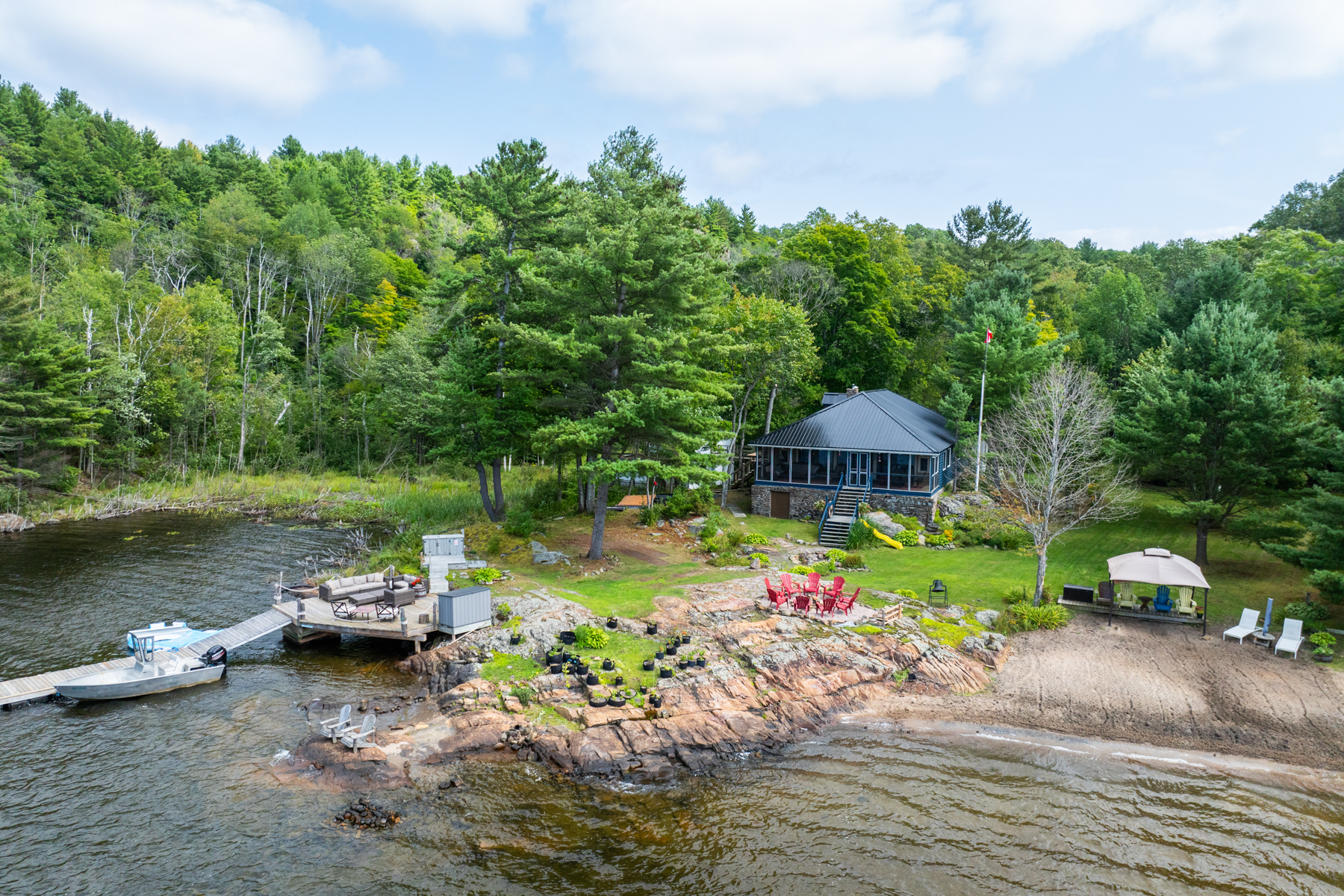 Aerial view of a blue cottage in a forested area, lakeside