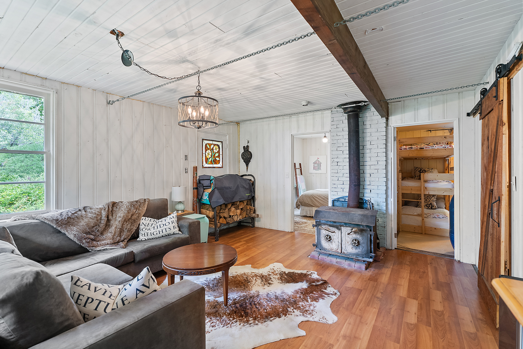 A white room with wood floors and a grey couch facing a woodstove