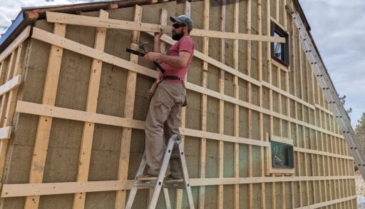 A man standing on a ladder, working on the side of a structure
