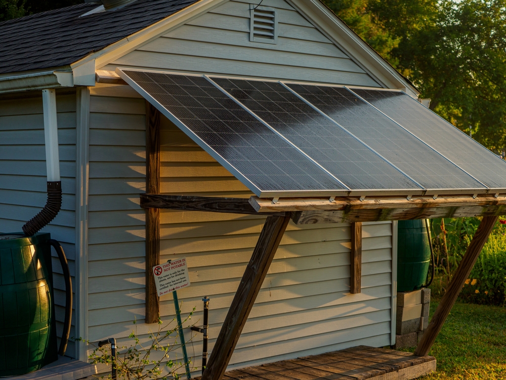 Off-grid setup with solar panels on a small shed in a garden setting. Green environment with rainwater collection barrels. Ideal for eco-friendly projects.