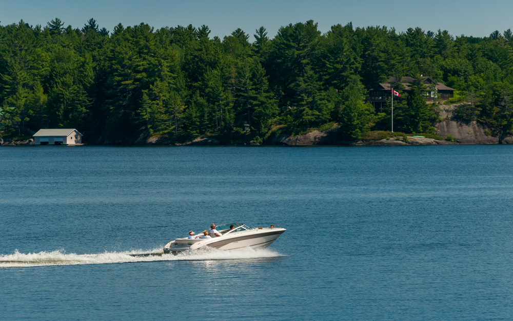 Boat moving along on Lake Muskoka lined with cottages and boathouses