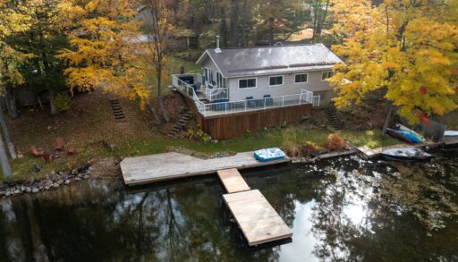 Aerial view of a small cottage beside a lake surrounded by fall trees