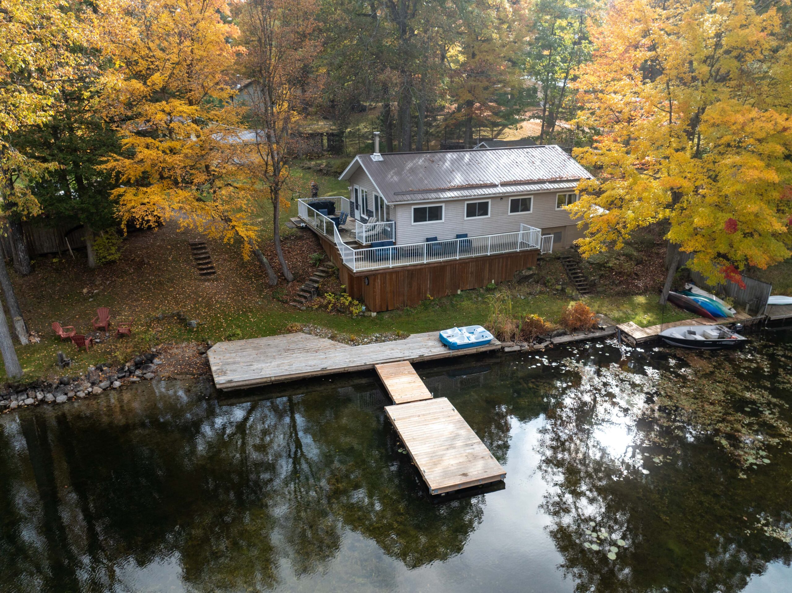 Aerial view of a small cottage beside a lake surrounded by fall trees