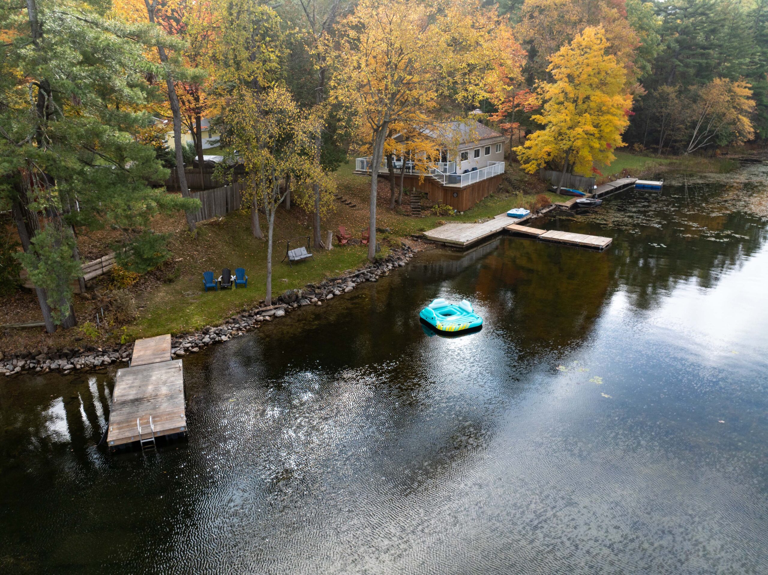 Aerial view of a small cottage beside a lake surrounded by fall trees