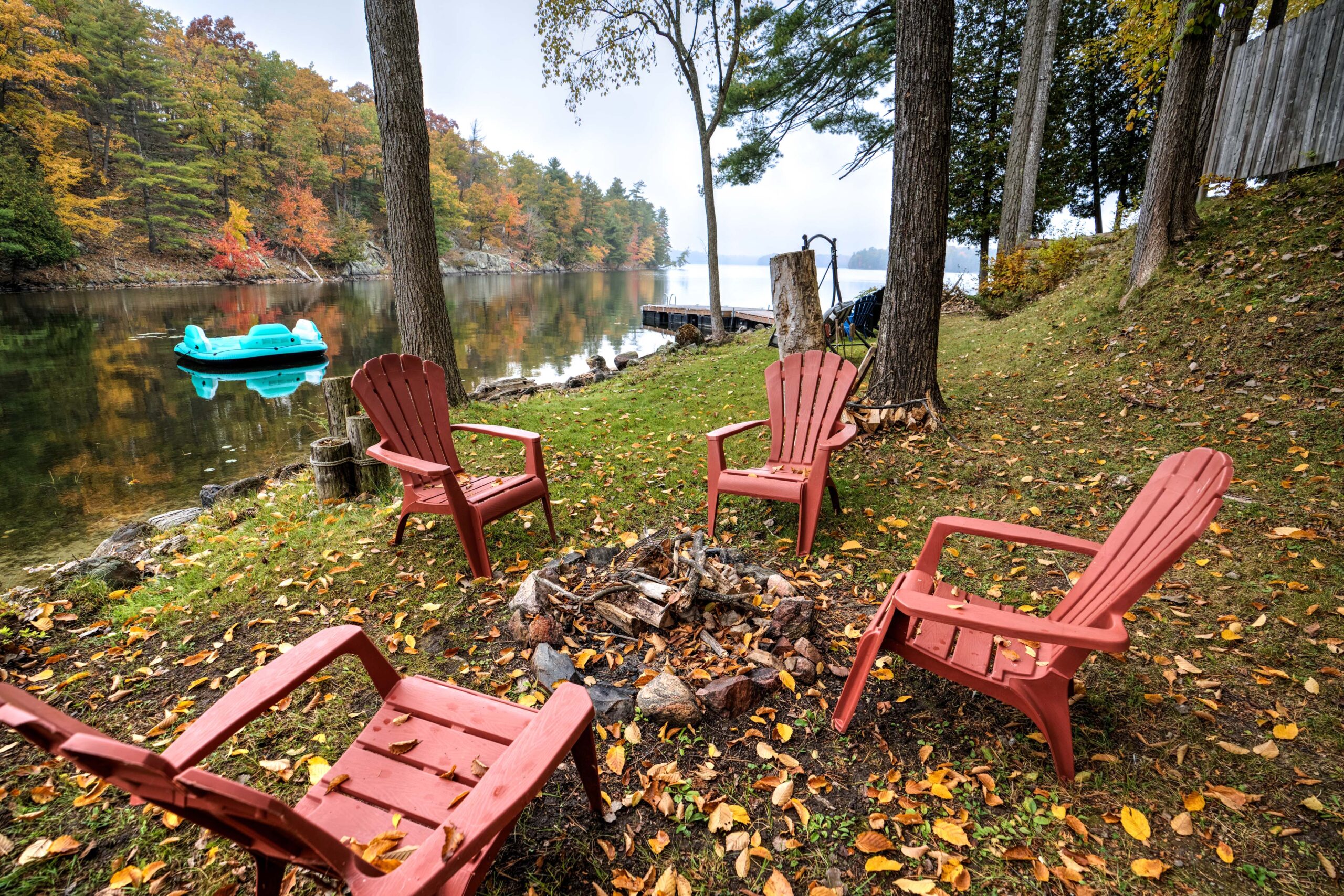 Four red Muskoka chairs sit around a waterfront fire pit