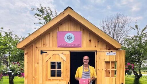 a photo of a man holding a box of butter tarts and standing outside of a shed