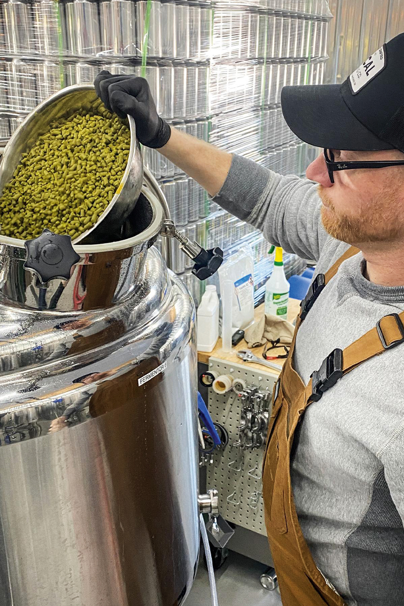 a person pouring hops into a fermentation tank