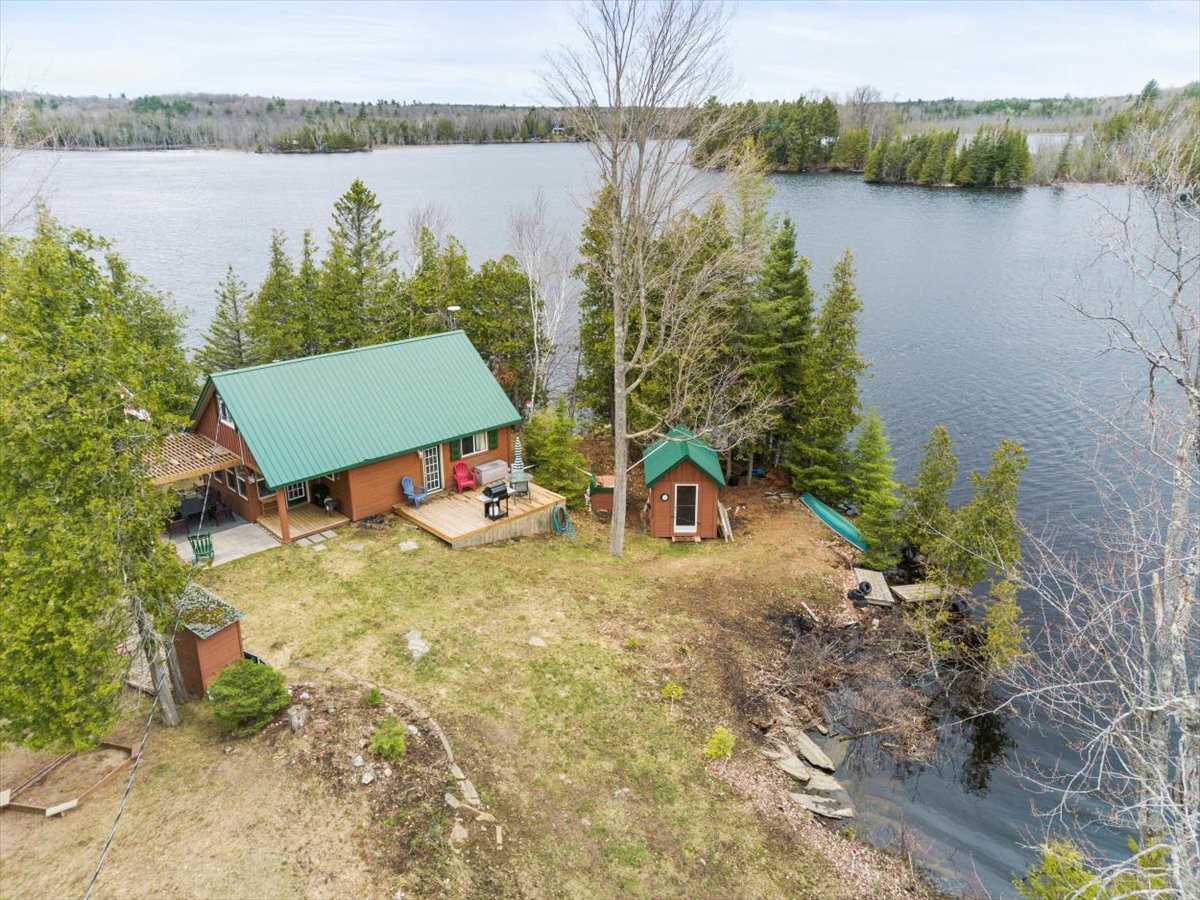 Aerial view of a log cabin with a green roof at the end of a lakeside peninsula