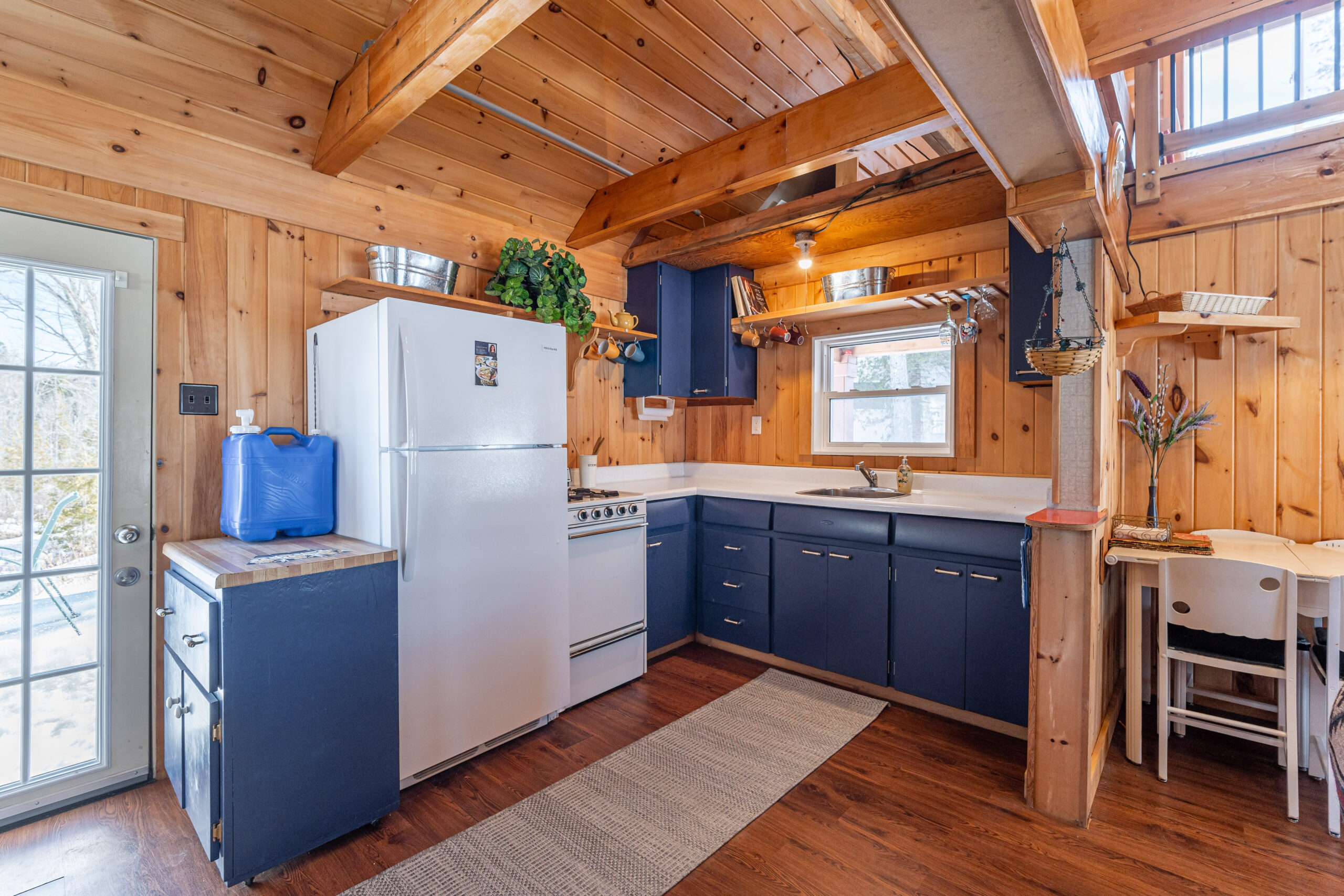 A small kitchen in a wood cabin with blue cabinets and white appliances