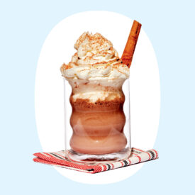 a photo of a creamy drink topped with whipped cream and a cinnamon stick in a glass mug