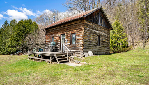A two-story log cabin in a grassy area