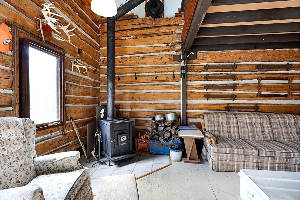 A wood stove and plaid couch face a coffee table in a wood-panelled room