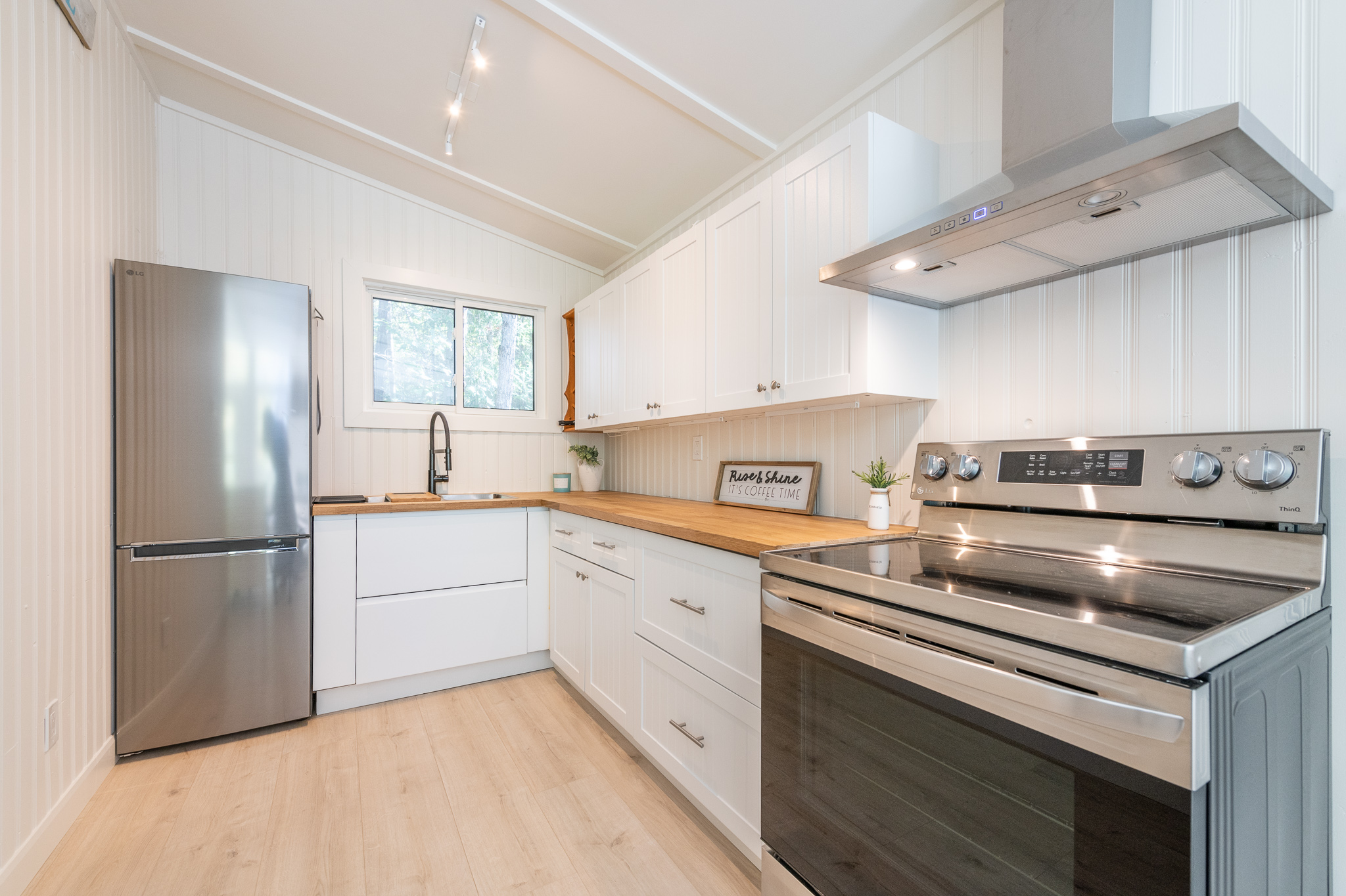 An L-shaped kitchen with stainless steel appliances, white cabinets, and a wood countertop