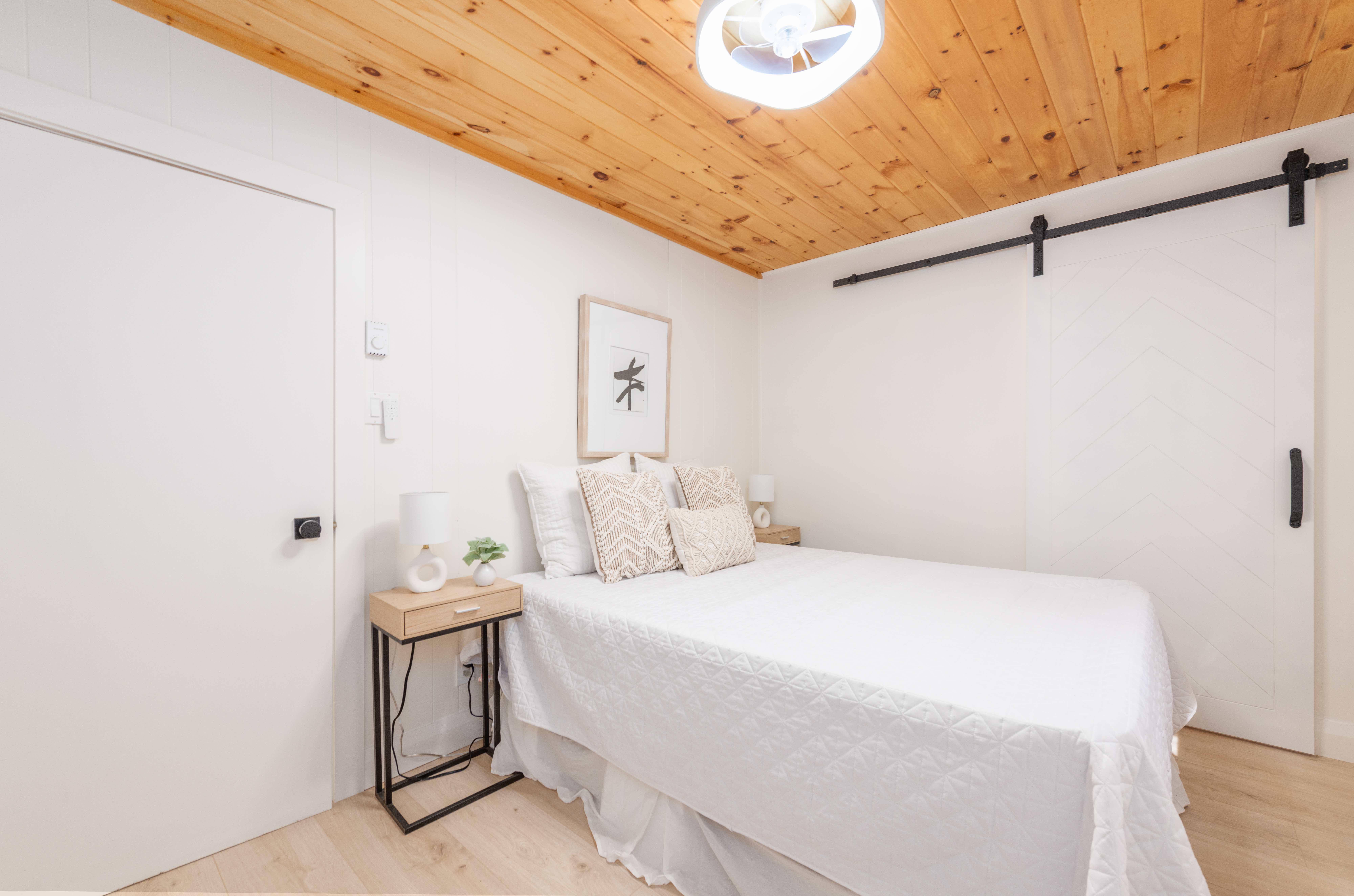 A white bed in a white room with a wood ceiling
