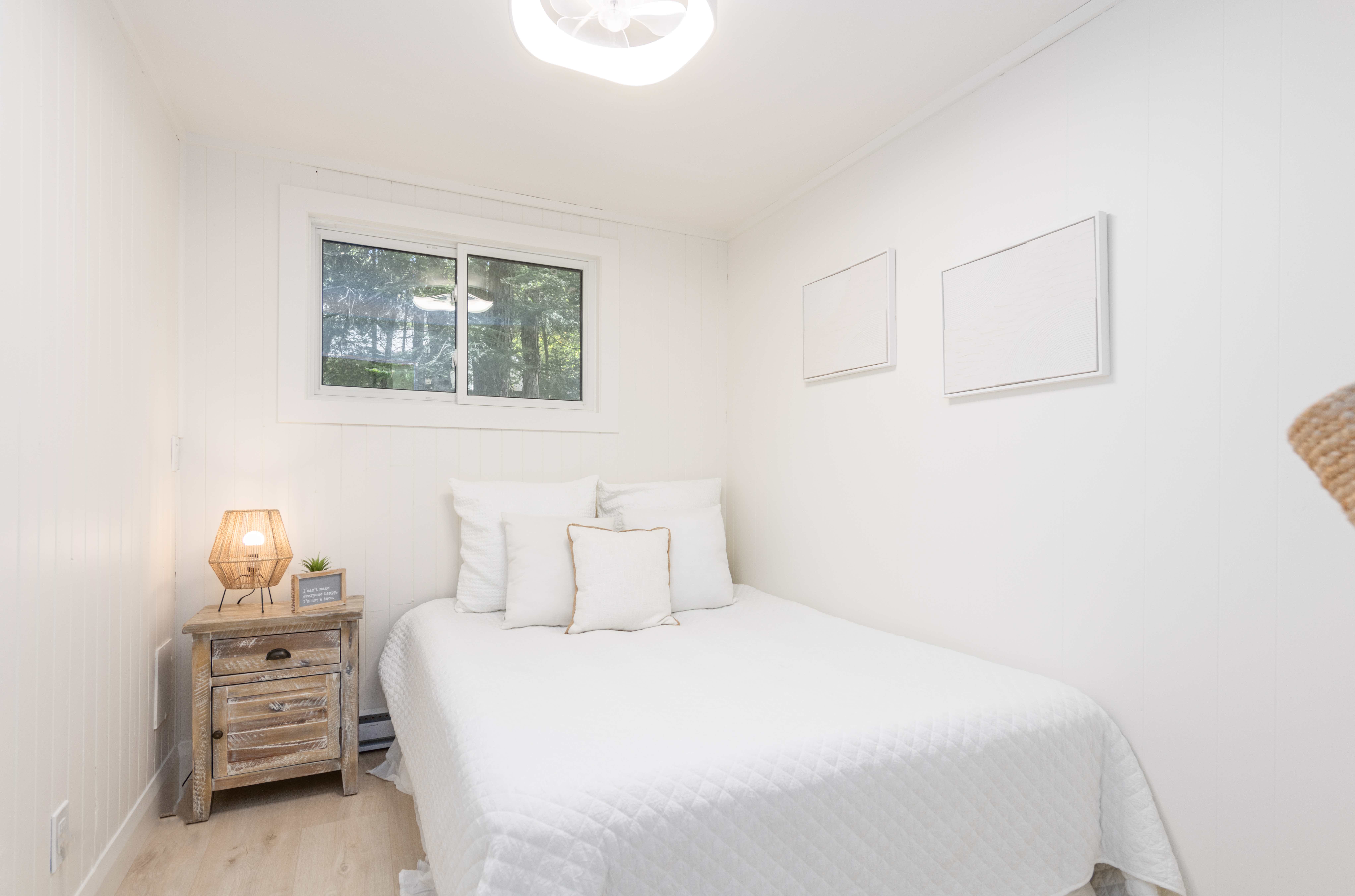 A white bed in a white room with a small window