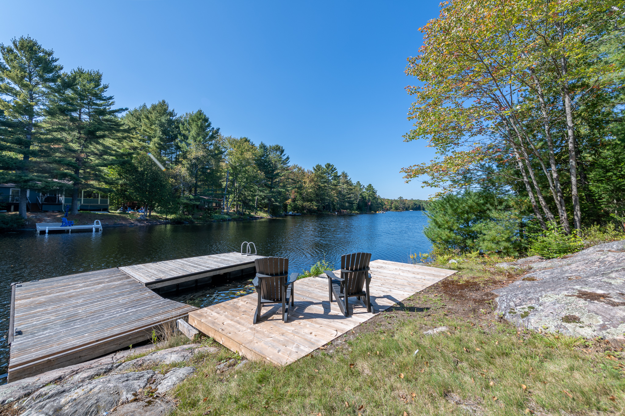 Two Muskoka chairs face a blue lake