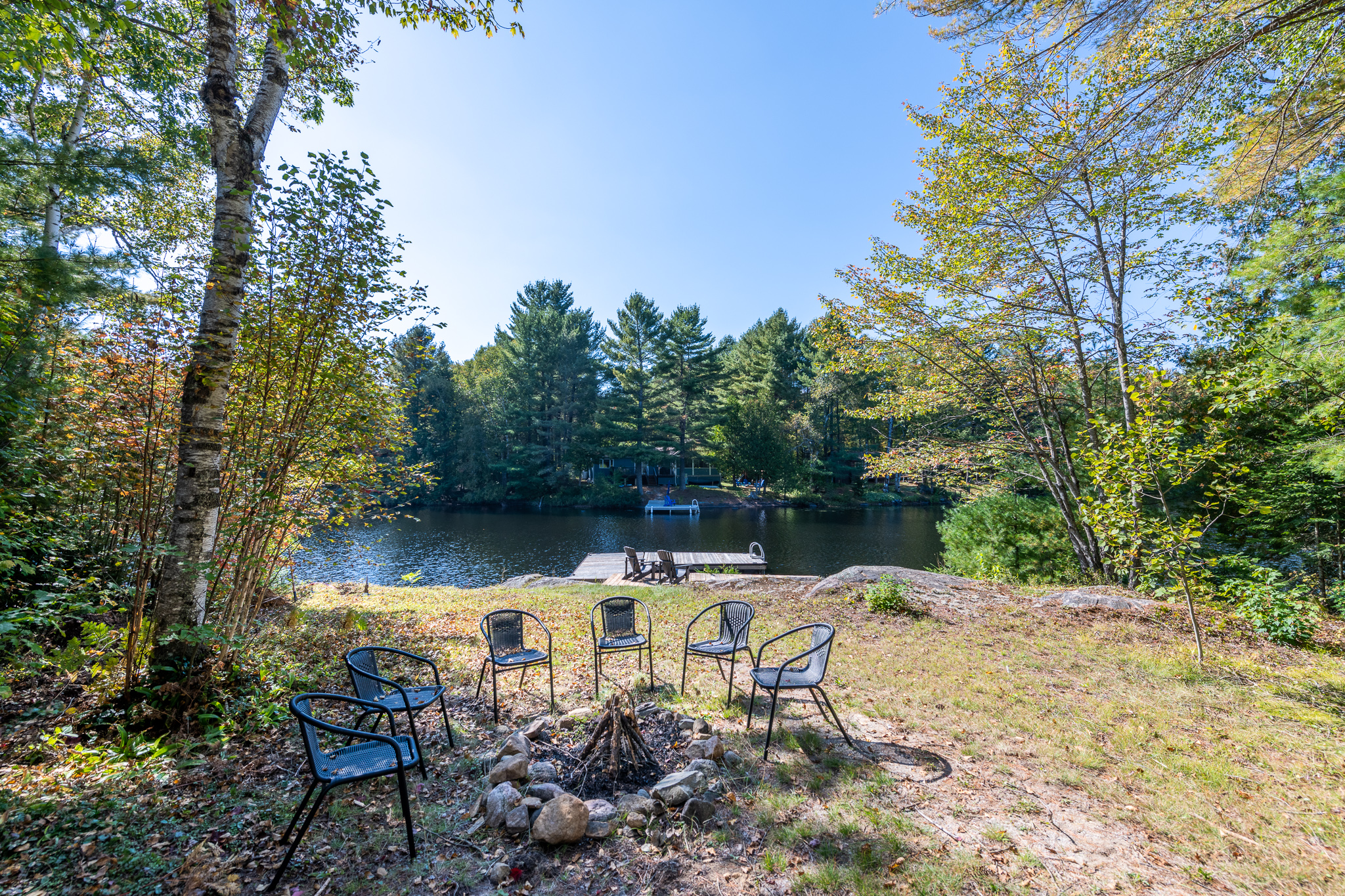 A small fire pit area with plastic chairs on a grassy area beside a lake