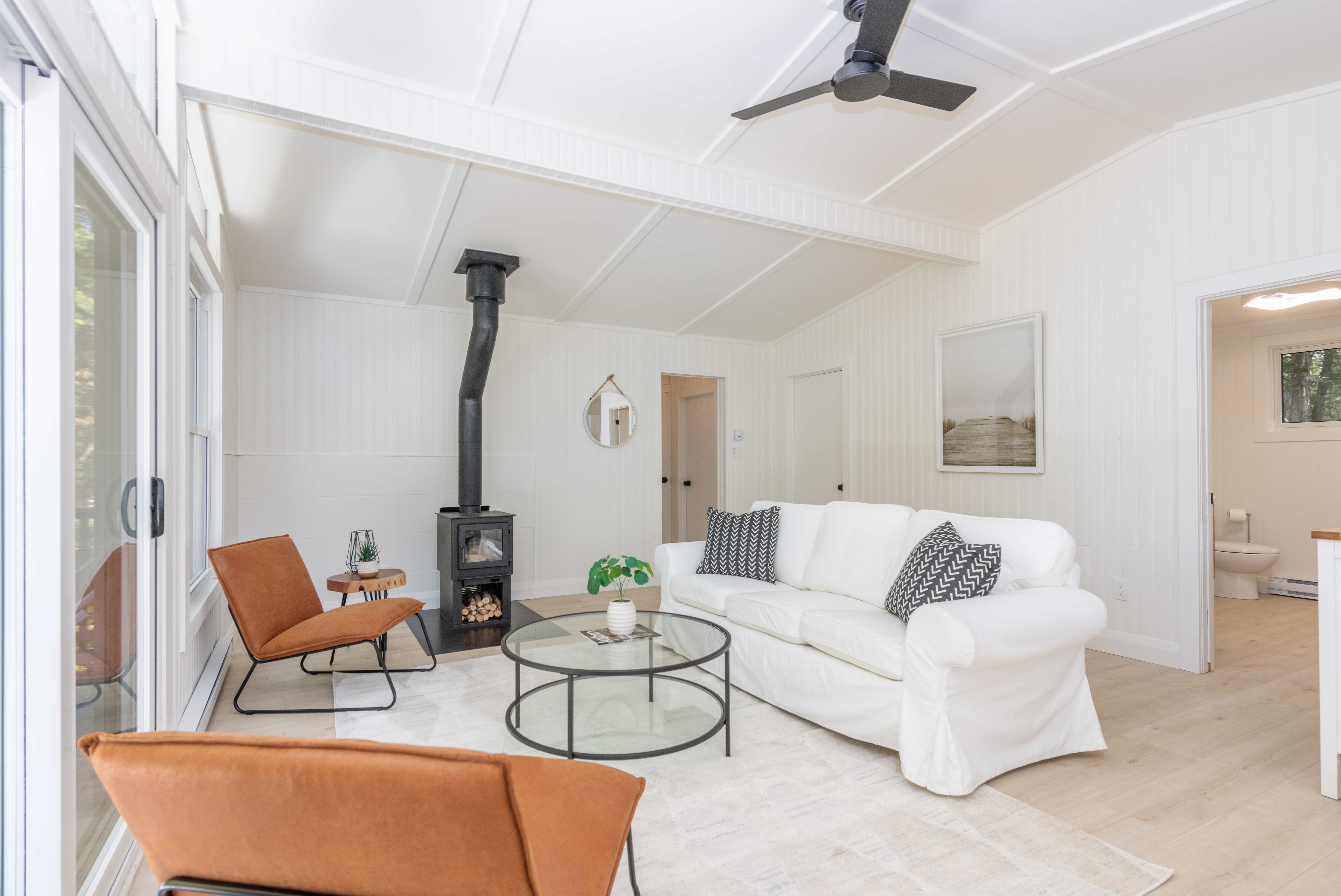 A plush white couch faces two orange chairs and a round glass table. To the left, a wood stove