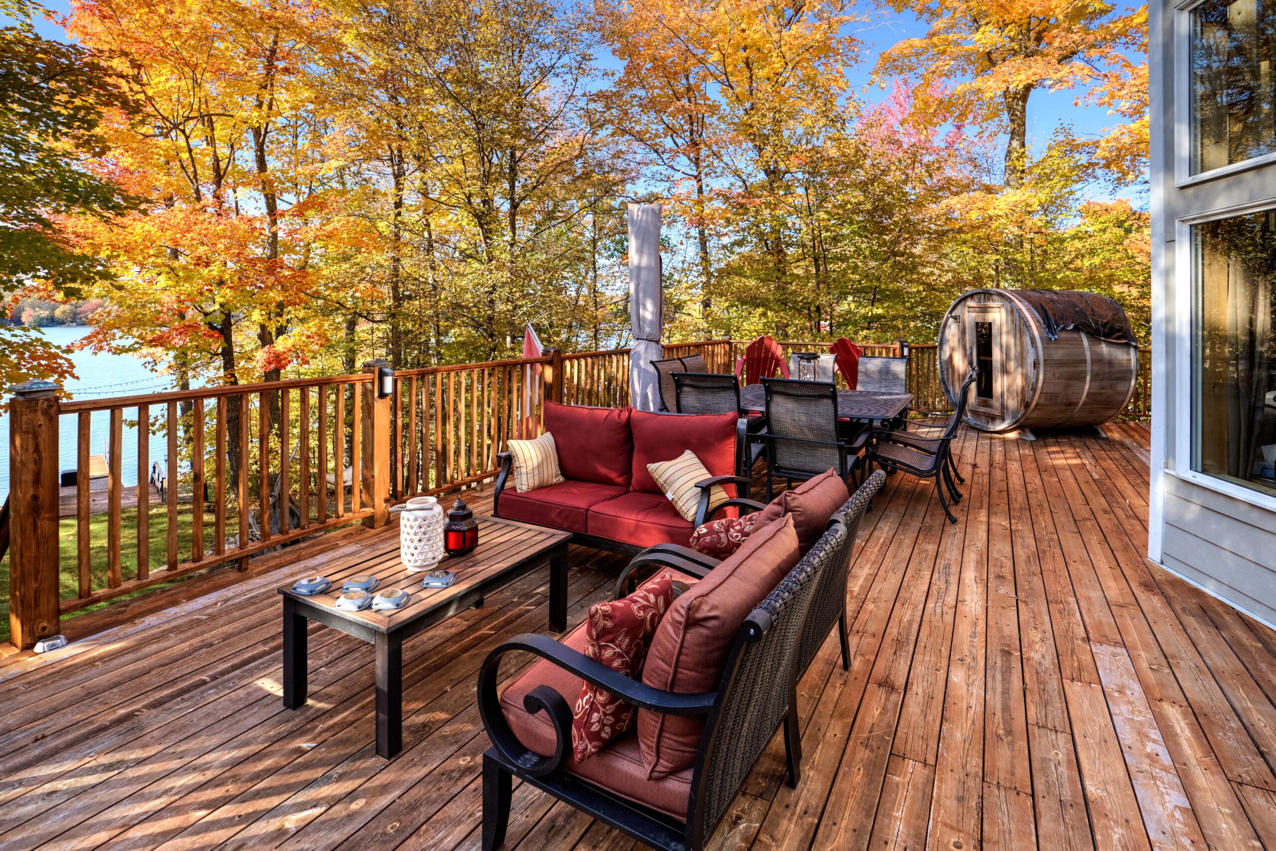 A modern patio set with red cushions. Autumn trees sit behind.
