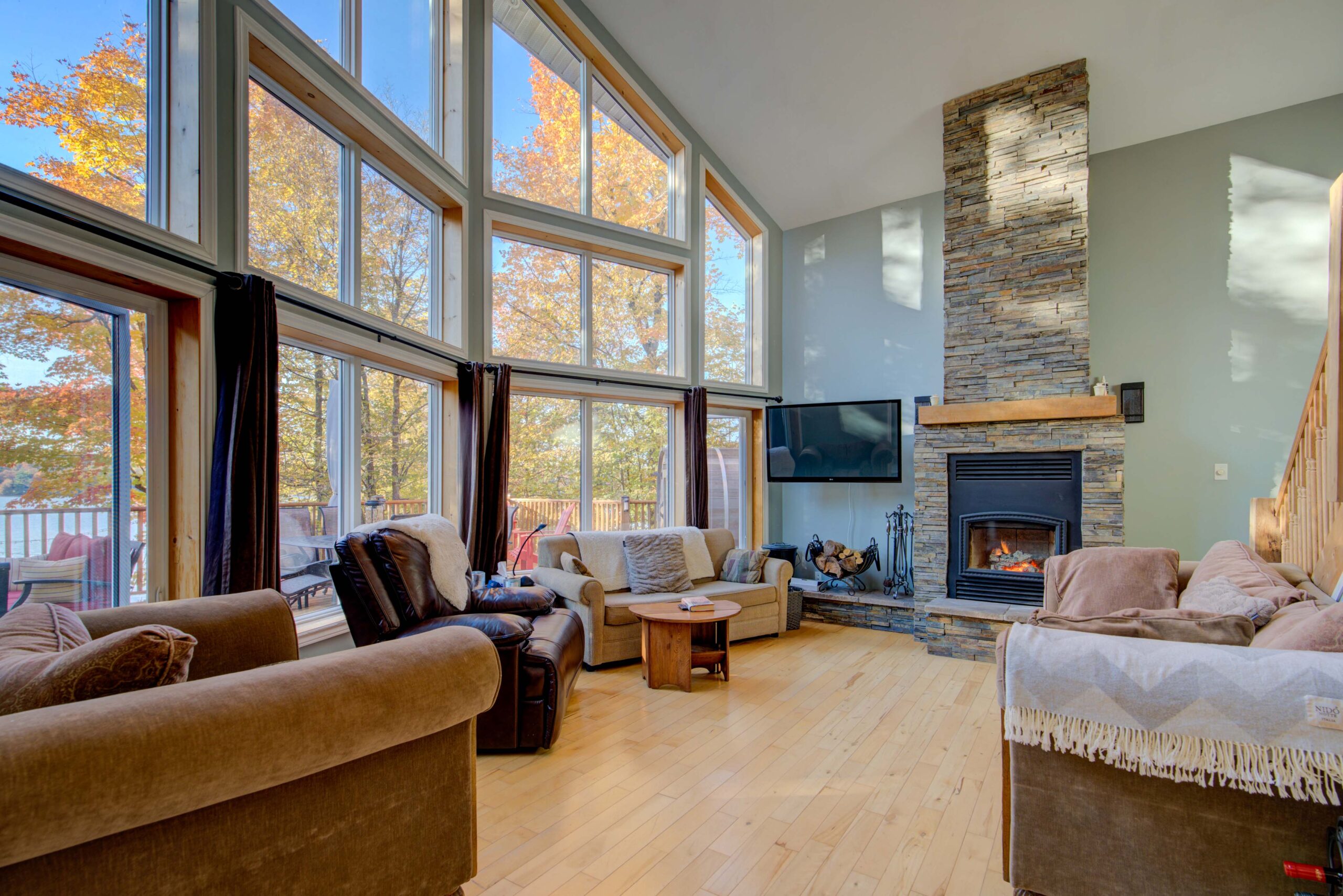 Couches face each other in a large living area with vaulted ceilings and floor-to-ceiling windows. A stone fireplace is on the far wall