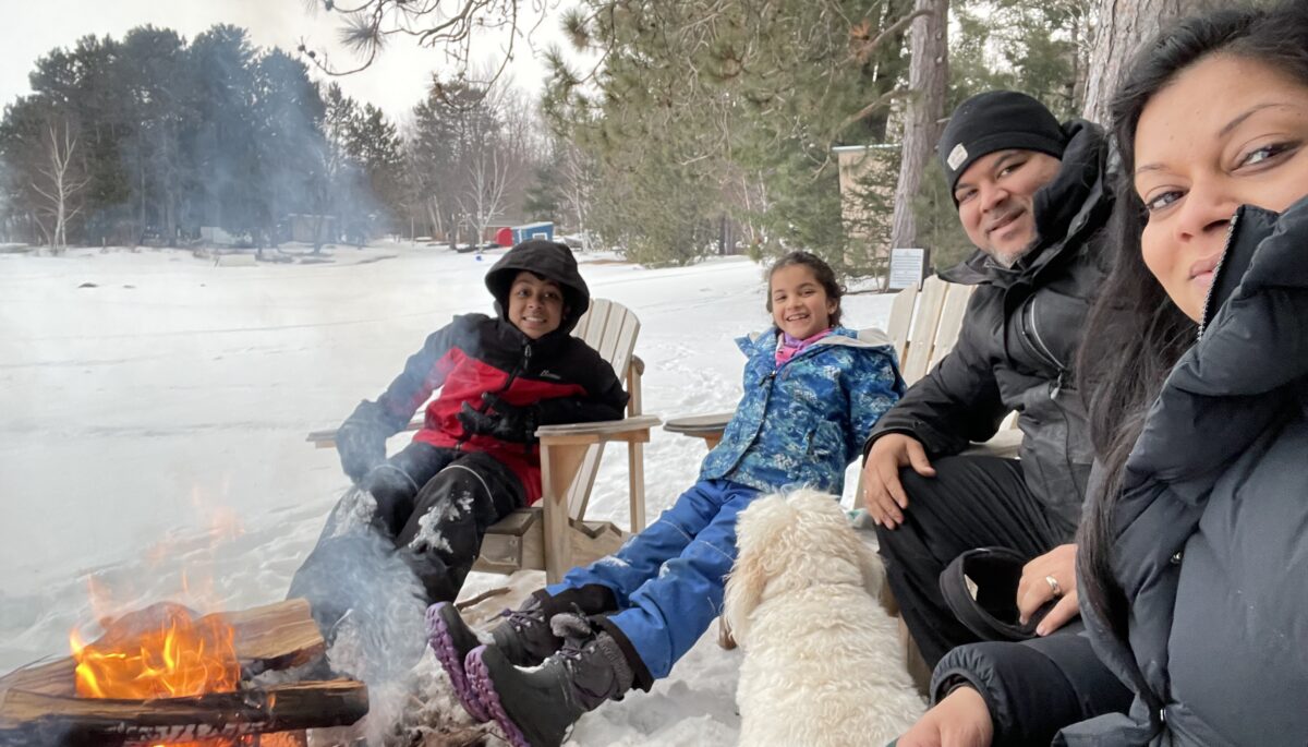 a family of four sit around a campfire in winter