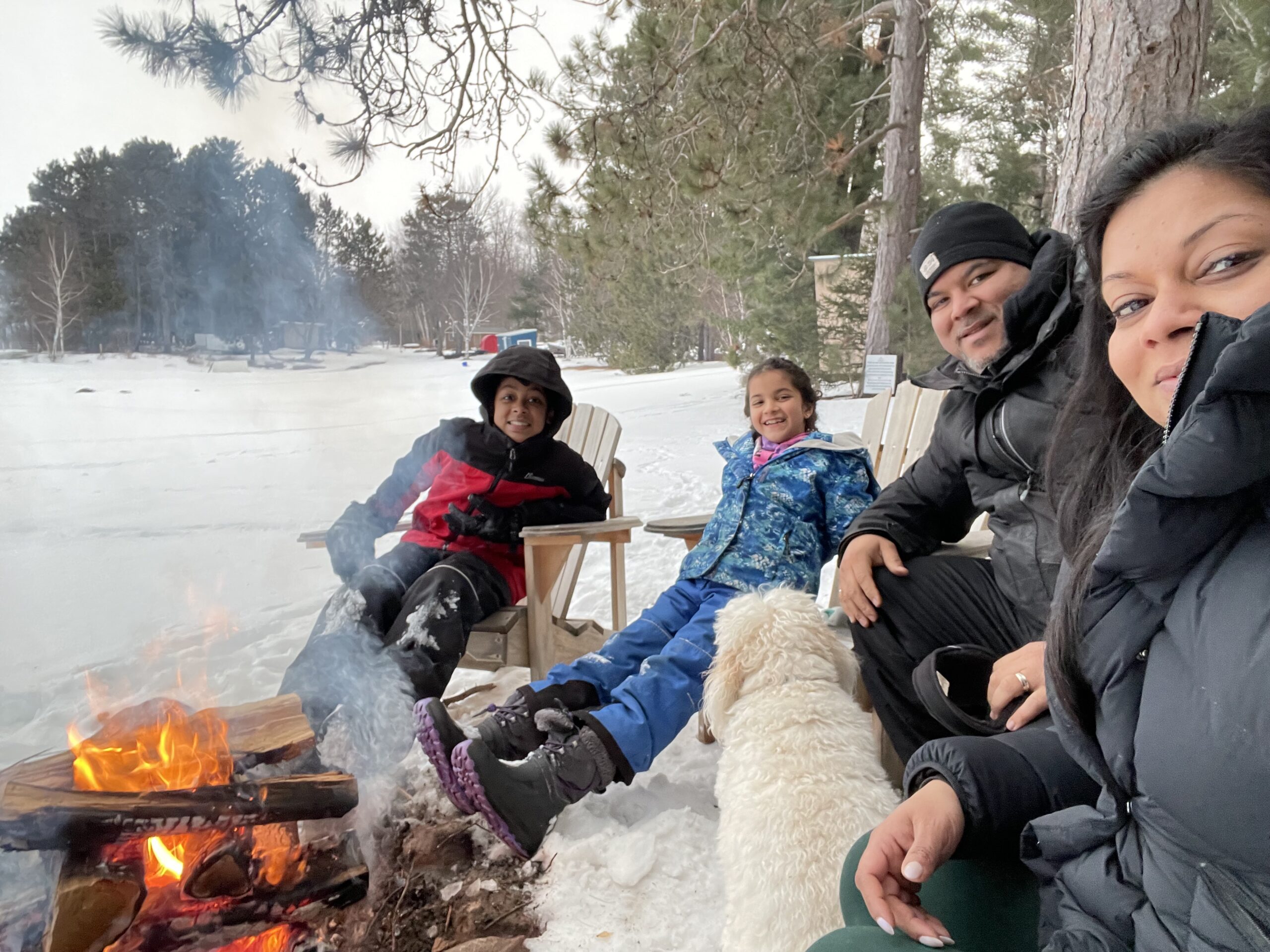 a family of four sit around a campfire in winter