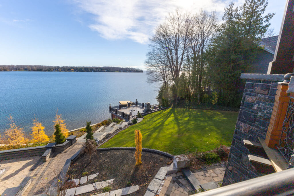 A spacious stone patio leads down to a blue lake